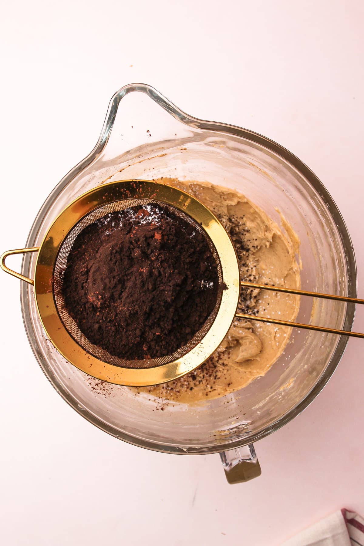 A fine-mesh strainer filled with cocoa set over a stand mixer bowl with dough for chocolate shortbread cookies.