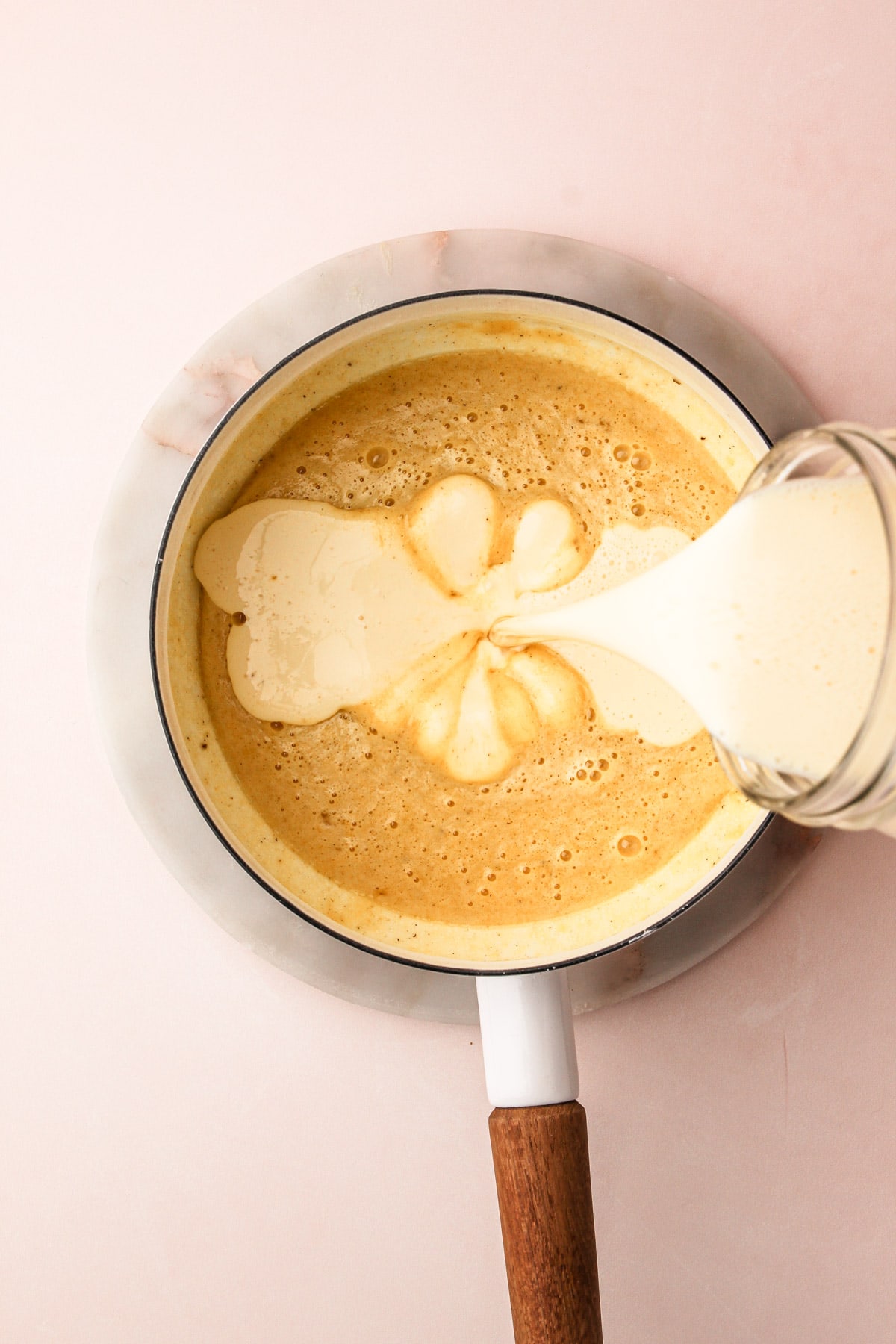 Eggnog pouring from a jar into a saucepan of ingredients for eggnog cream pie filling.