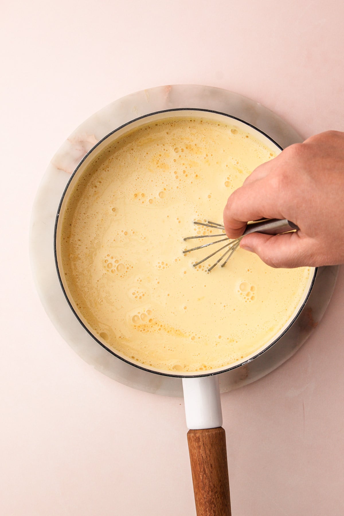 A hand whisking together ingredients for eggnog cream pie filling in a saucepan.