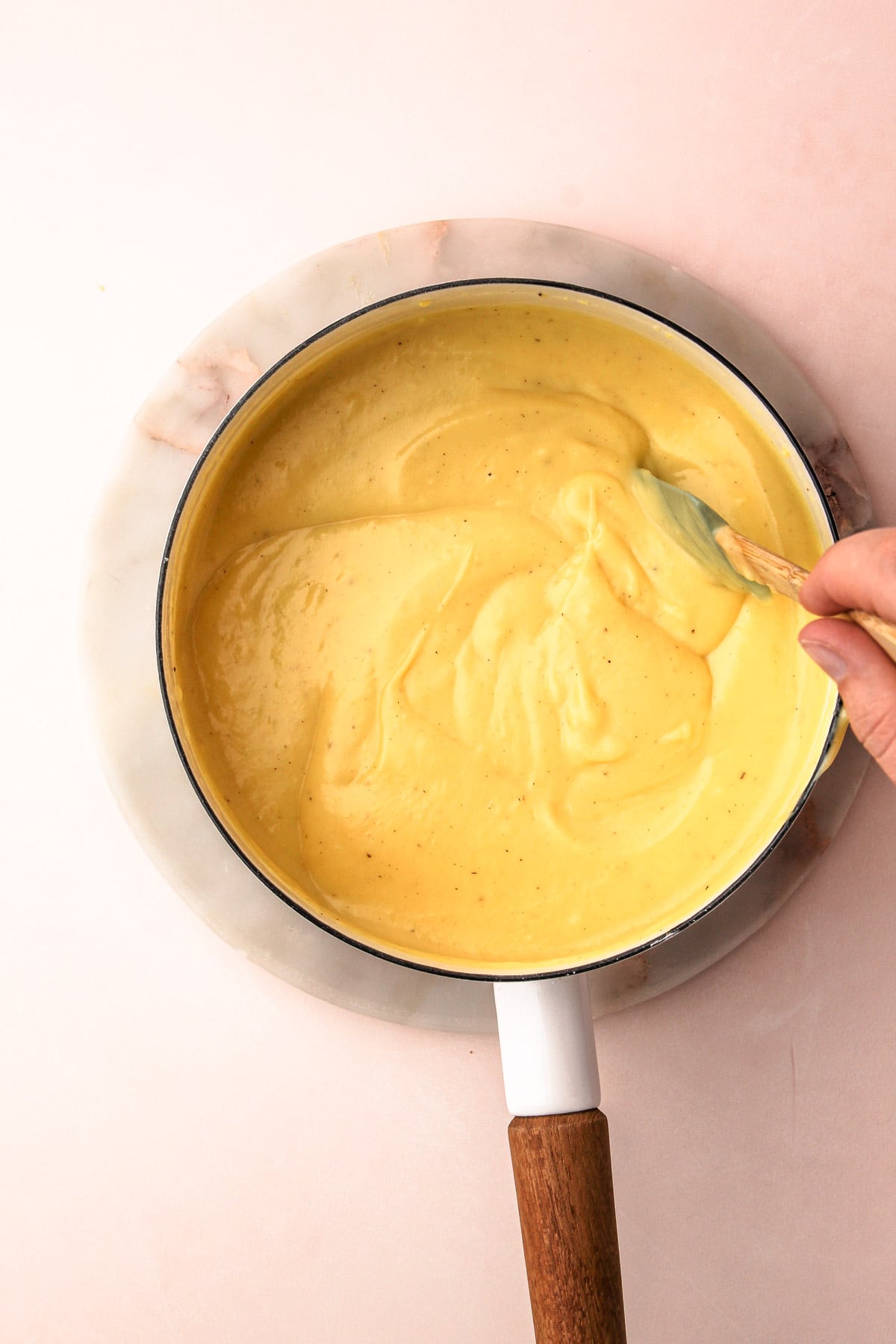 A hand using a rubber spatula to stir together eggnog cream pie filling in a saucepan.