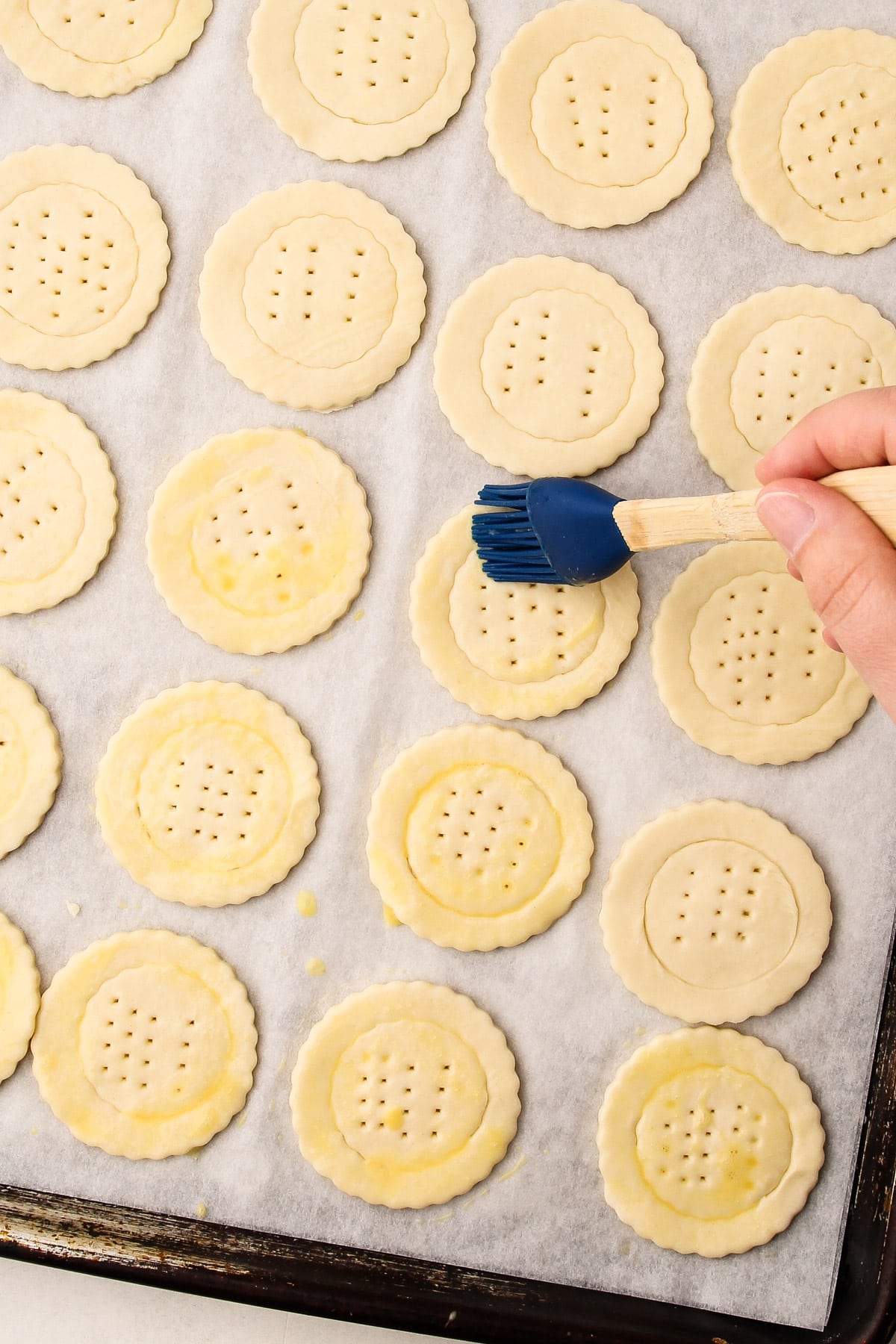 Puff pastry circles on a parchment lined sheetpan with a circle indent and fork marks in the middle getting a brush of eggwash.