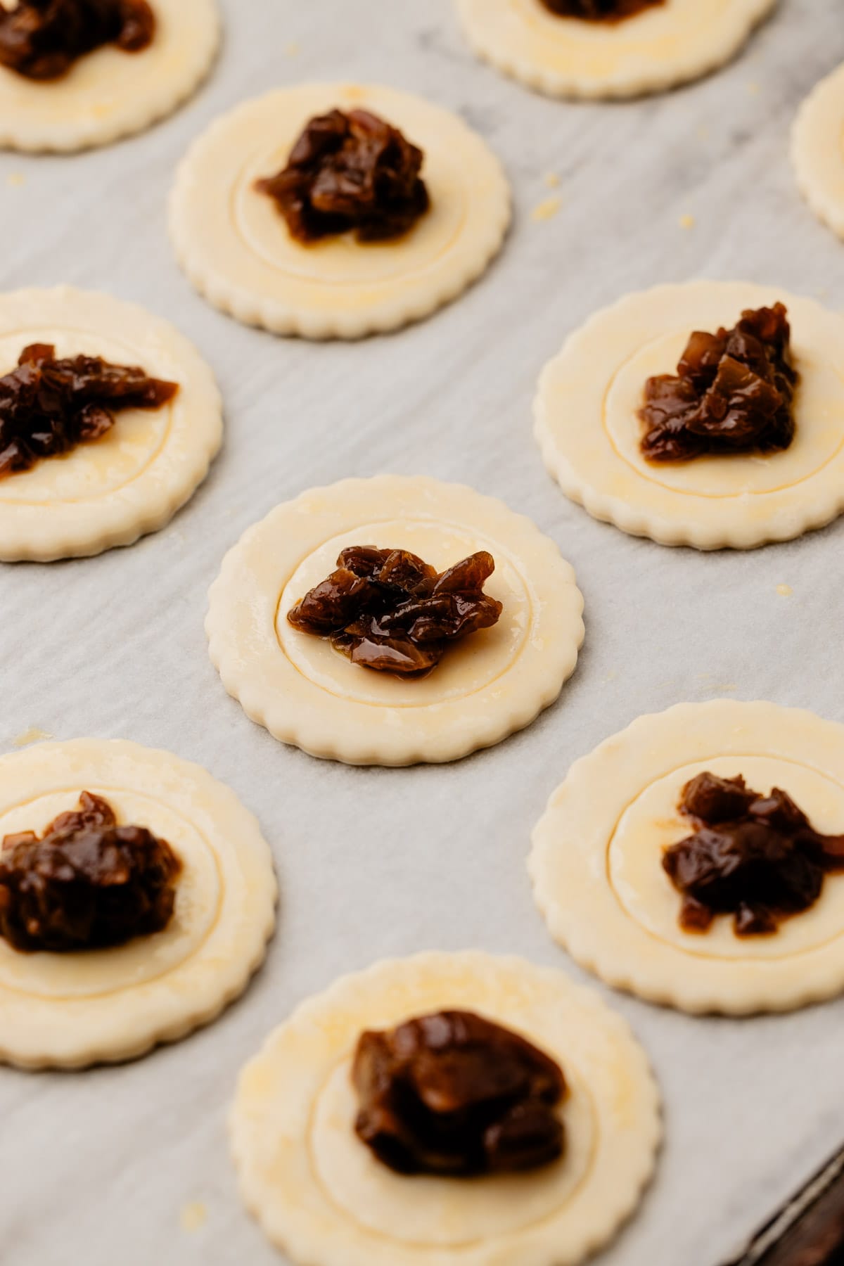 Small pieces of prepared puff pastry with caramelized onion on it before going into the oven.