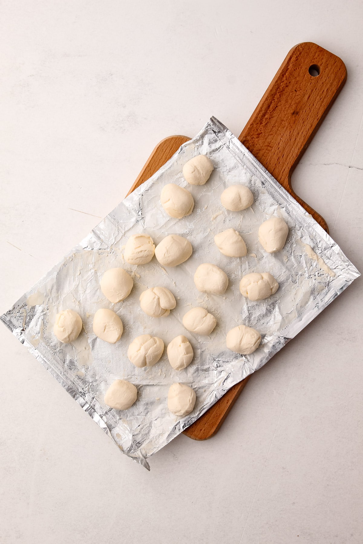 Rounded balls of cream cheese on foil on a cutting board for puff pastry pepper jelly bites.