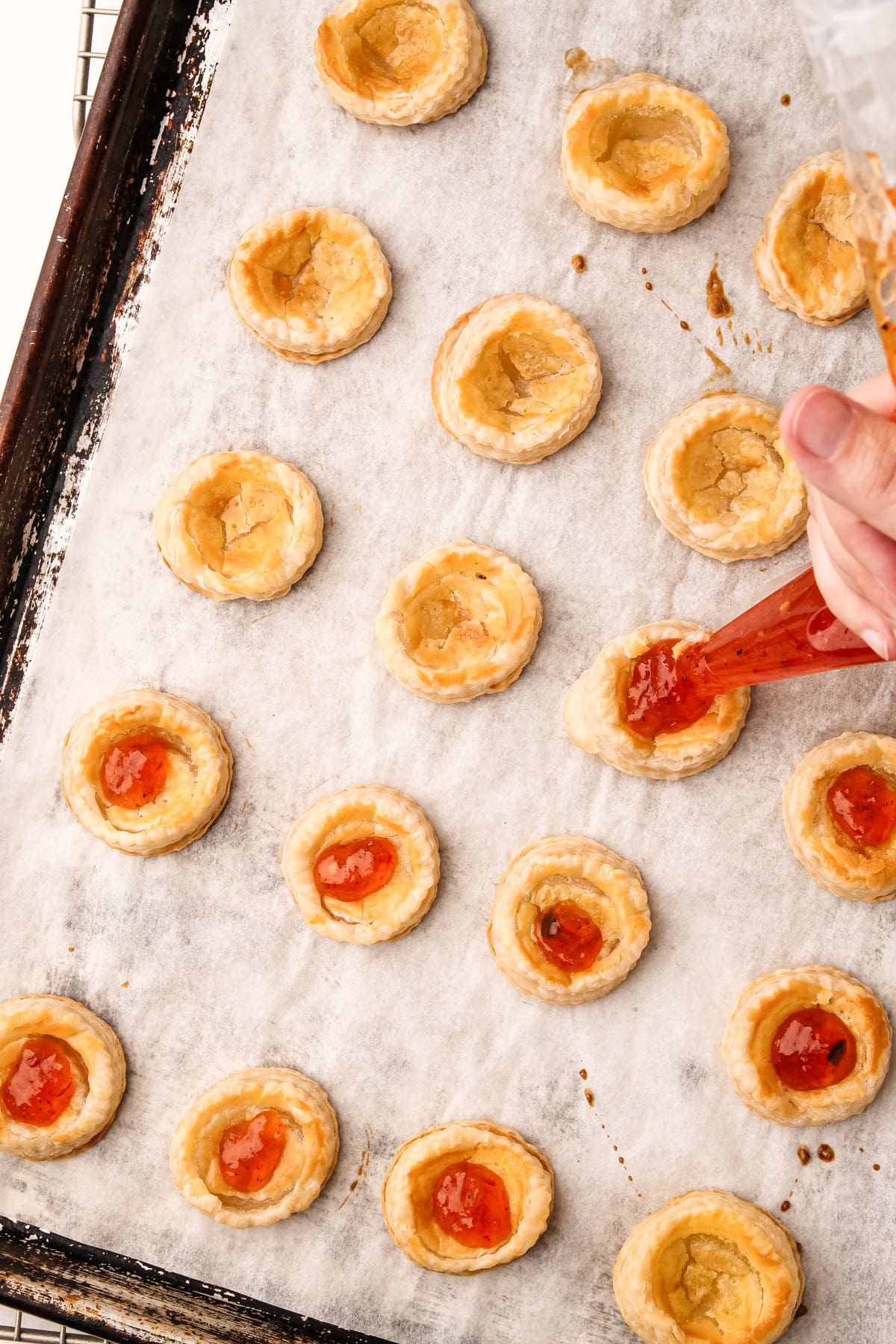 A hand using a pastry bag to fill puff pastry rounds with hot pepper jelly for cream cheese and pepper jelly bites.