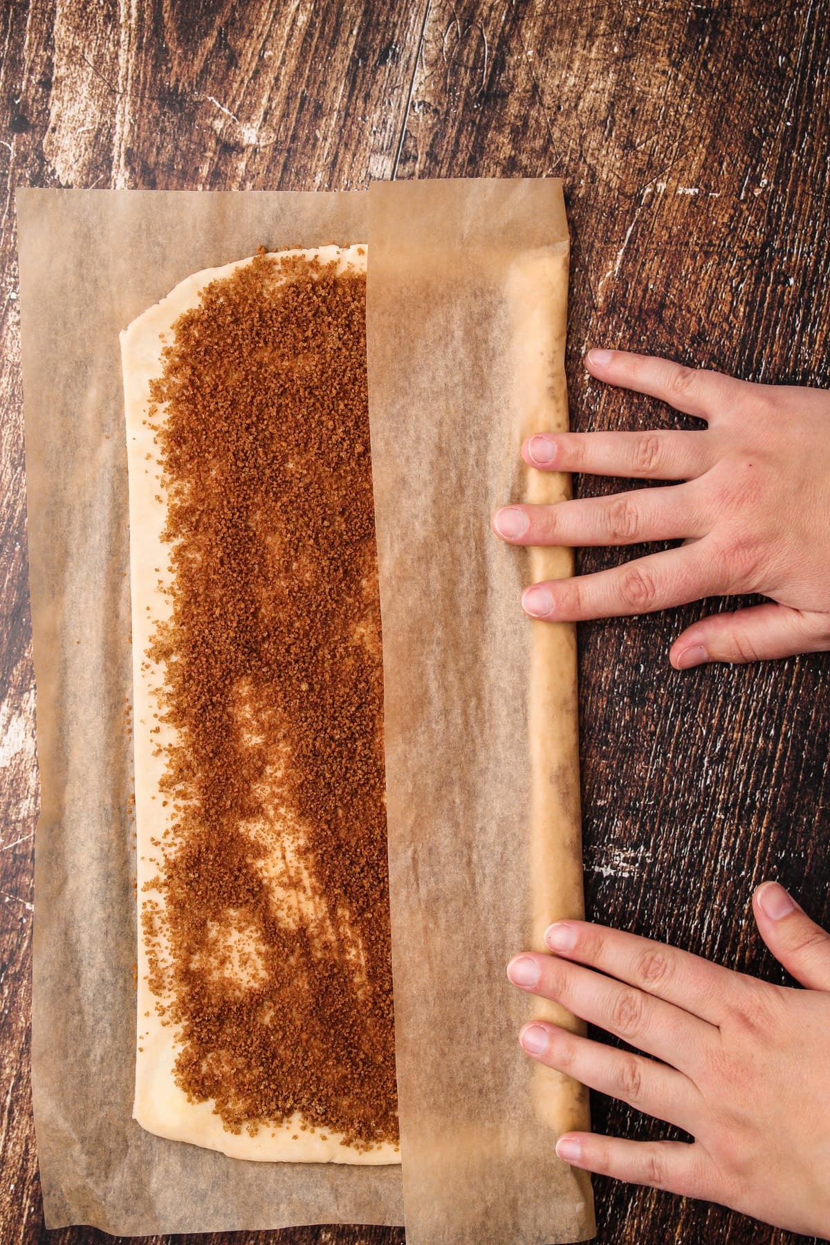 Using parchment as an aid to roll up pie crust cinnamon roll dough.