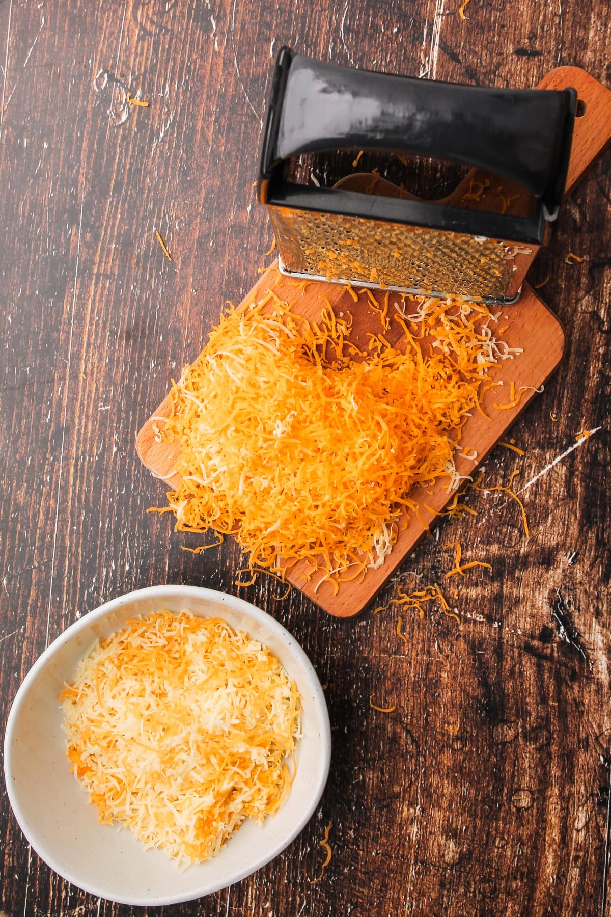 Shredded cheese in a bowl and on a cutting board with a box grater for puff pastry cheese twists.