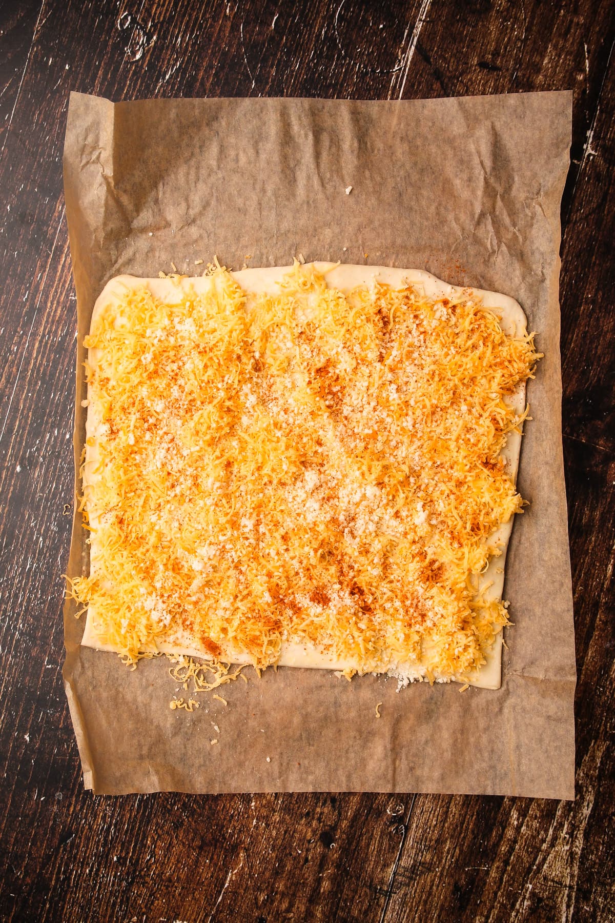 A square of puff pastry covered with shredded cheese for puff pastry cheese twists.