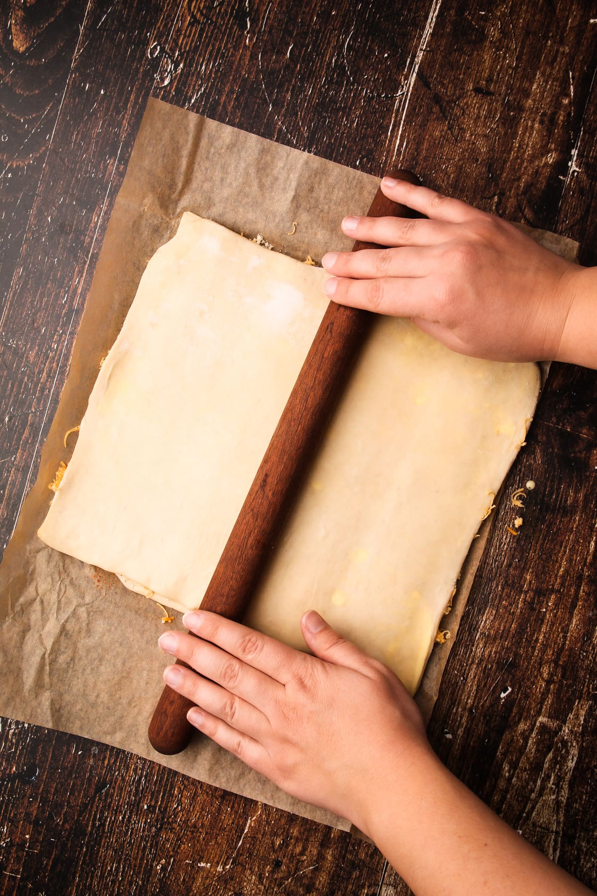 Two hands using a rolling pin to roll out pastry for puff pastry cheese straws.