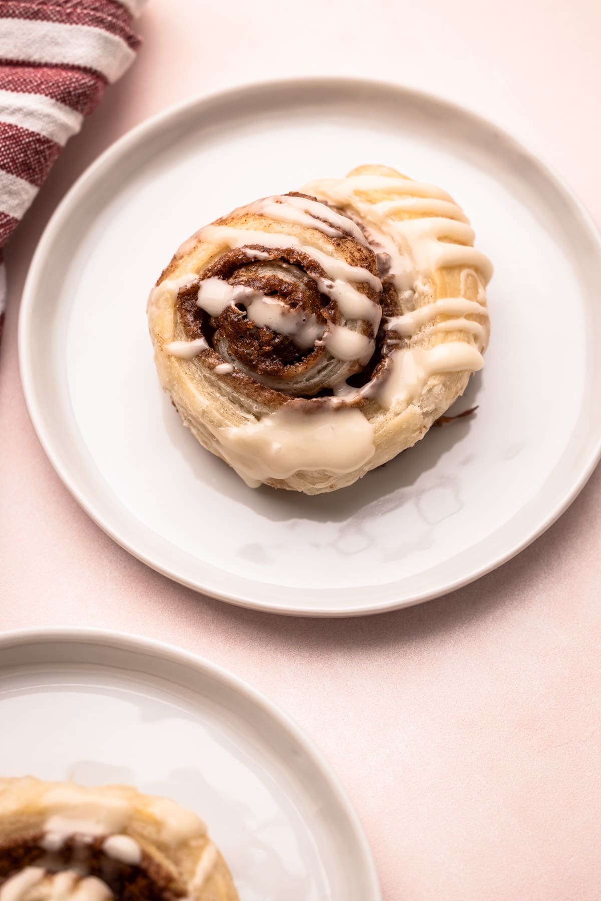 A baked and glazed puff pastry cinnamon roll on a plate.