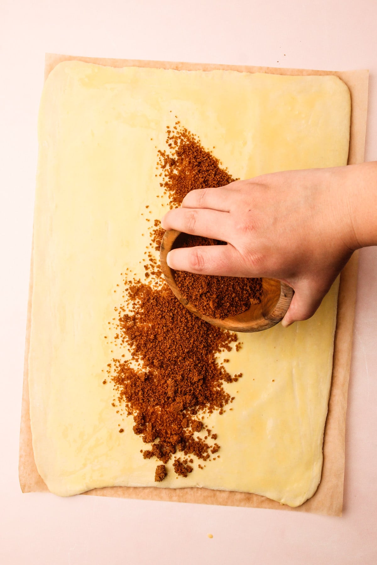 A hand sprinkling cinnamon filling onto puff pastry for puff pastry cinnamon rolls.