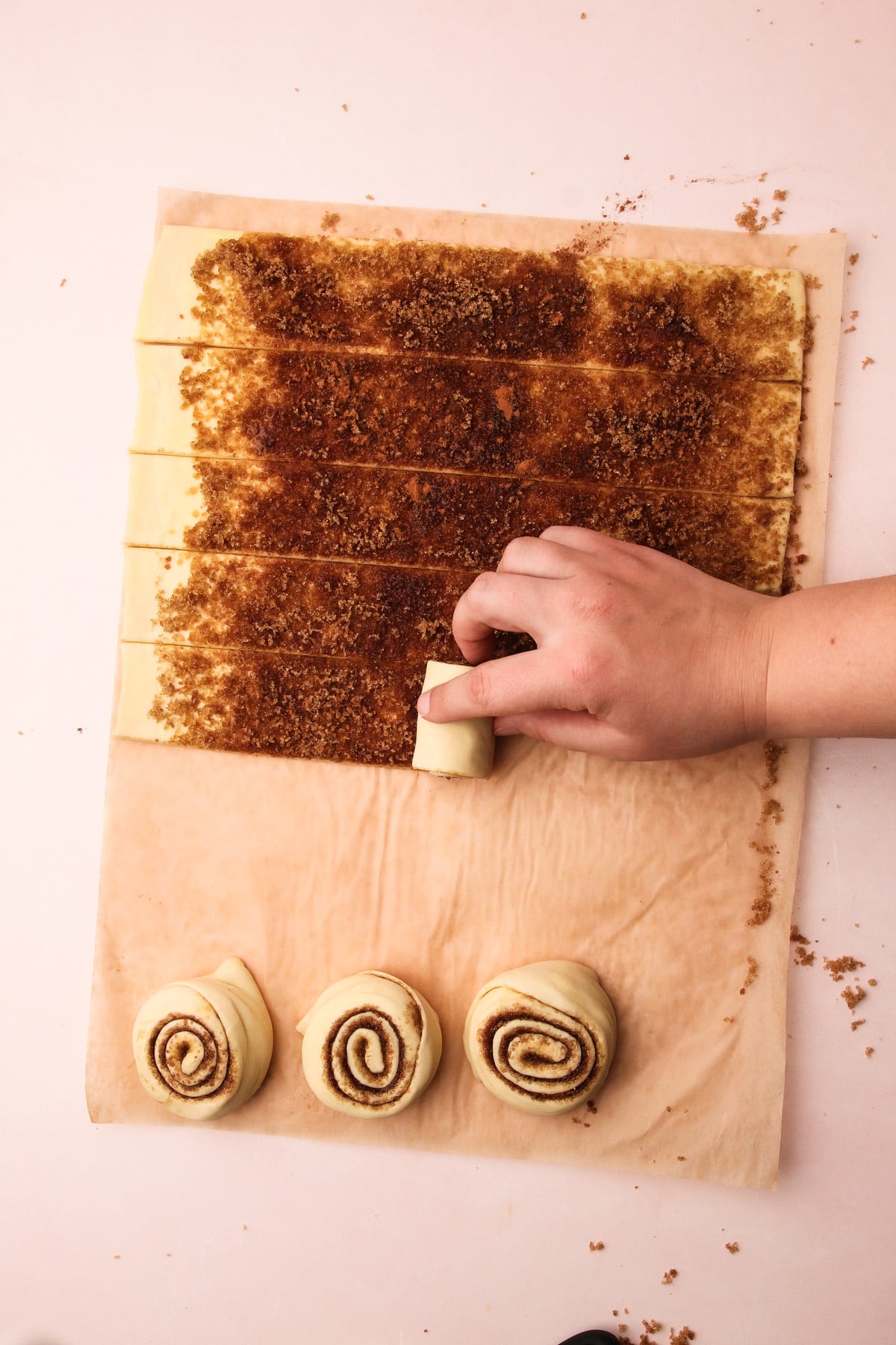 A rolling up a strip of cinnamon-covered puff pastry into a spiral for puff pastry cinnamon rolls.