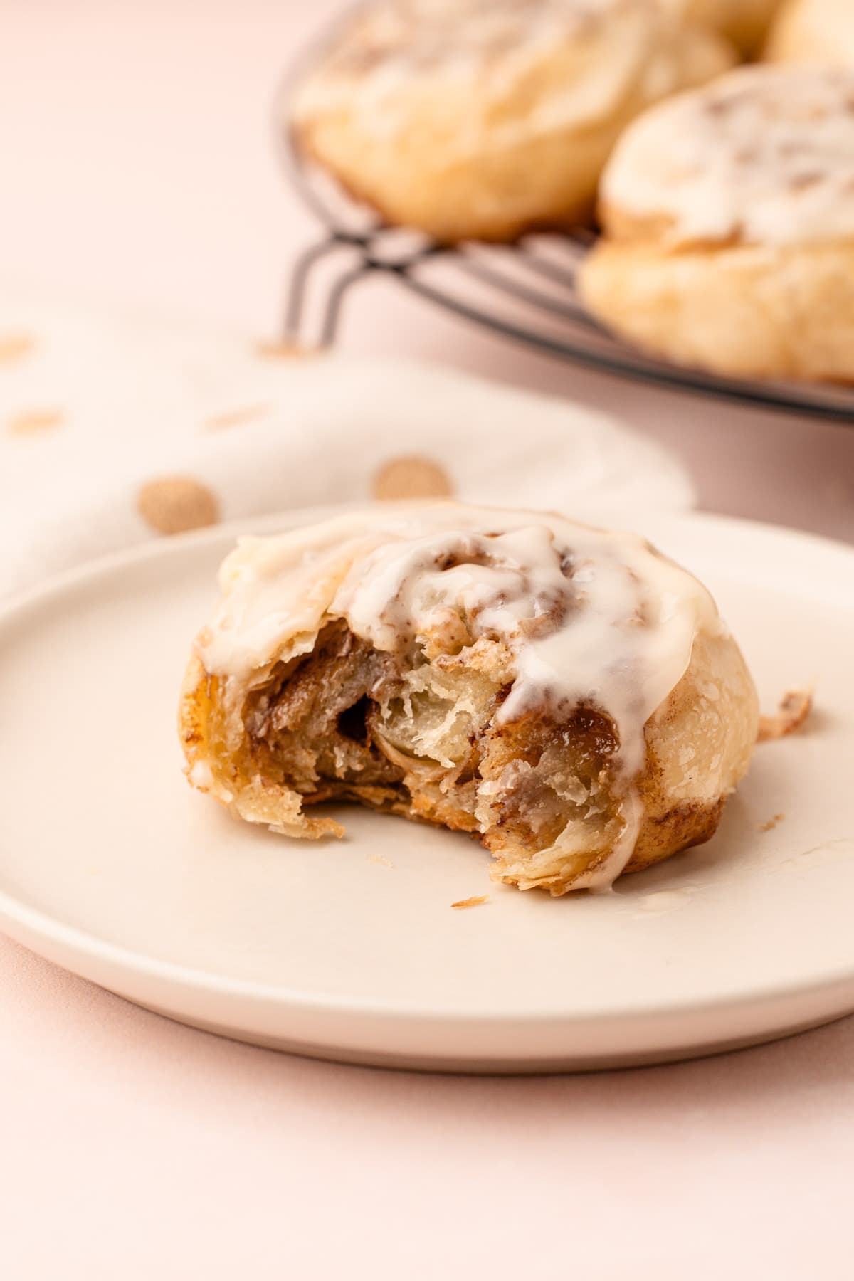 A baked and glazed puff pastry cinnamon roll on a plate, with a bite taken out of it.