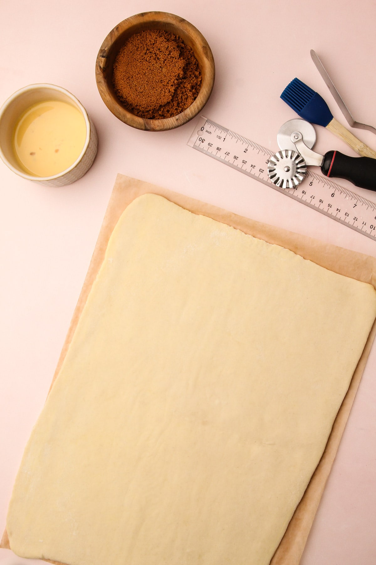 A sheet of puff pastry dough with small bowls of egg wash and cinnamon filling and shaping tools next to it for puff pastry cinnamon rolls.