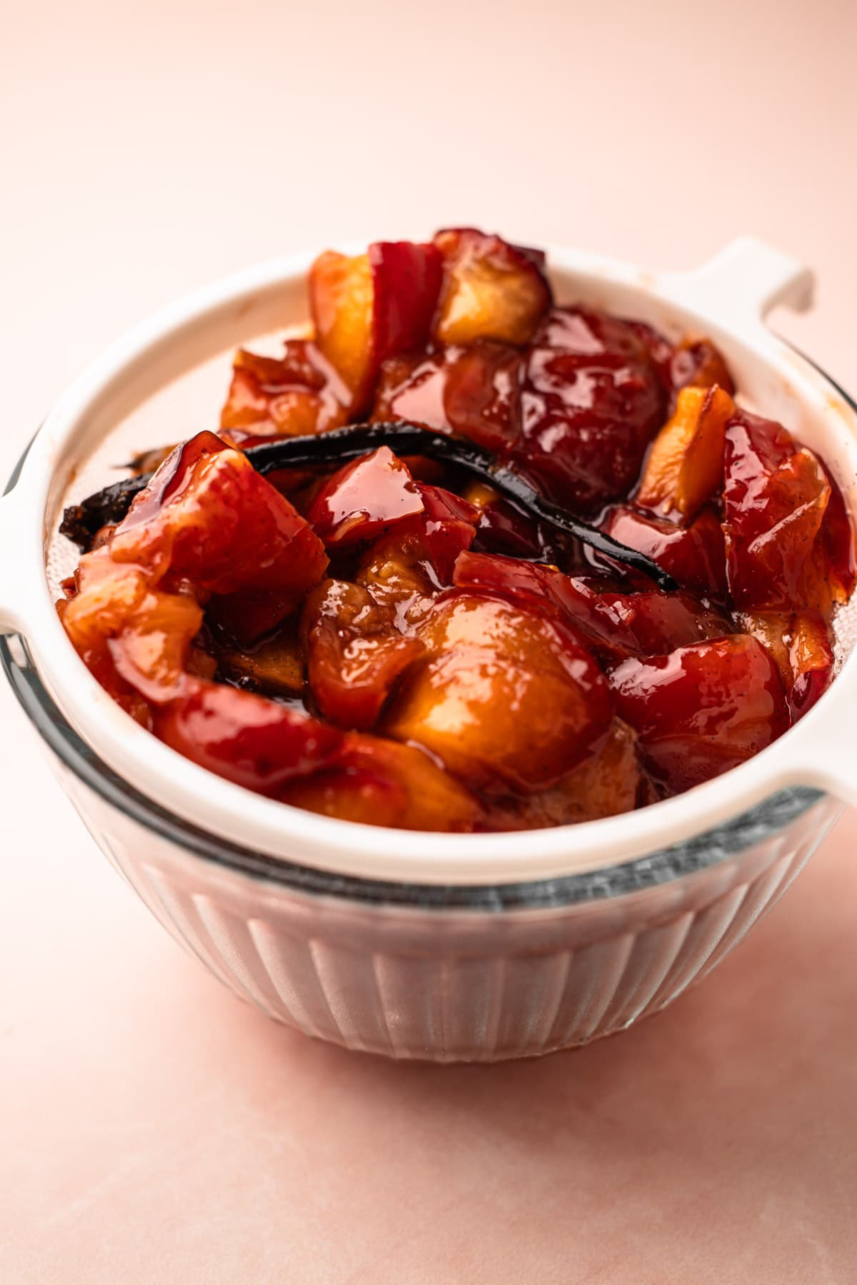 A fine-mesh strainer filled with roasted plums and set over a bowl for roasted plum pie.
