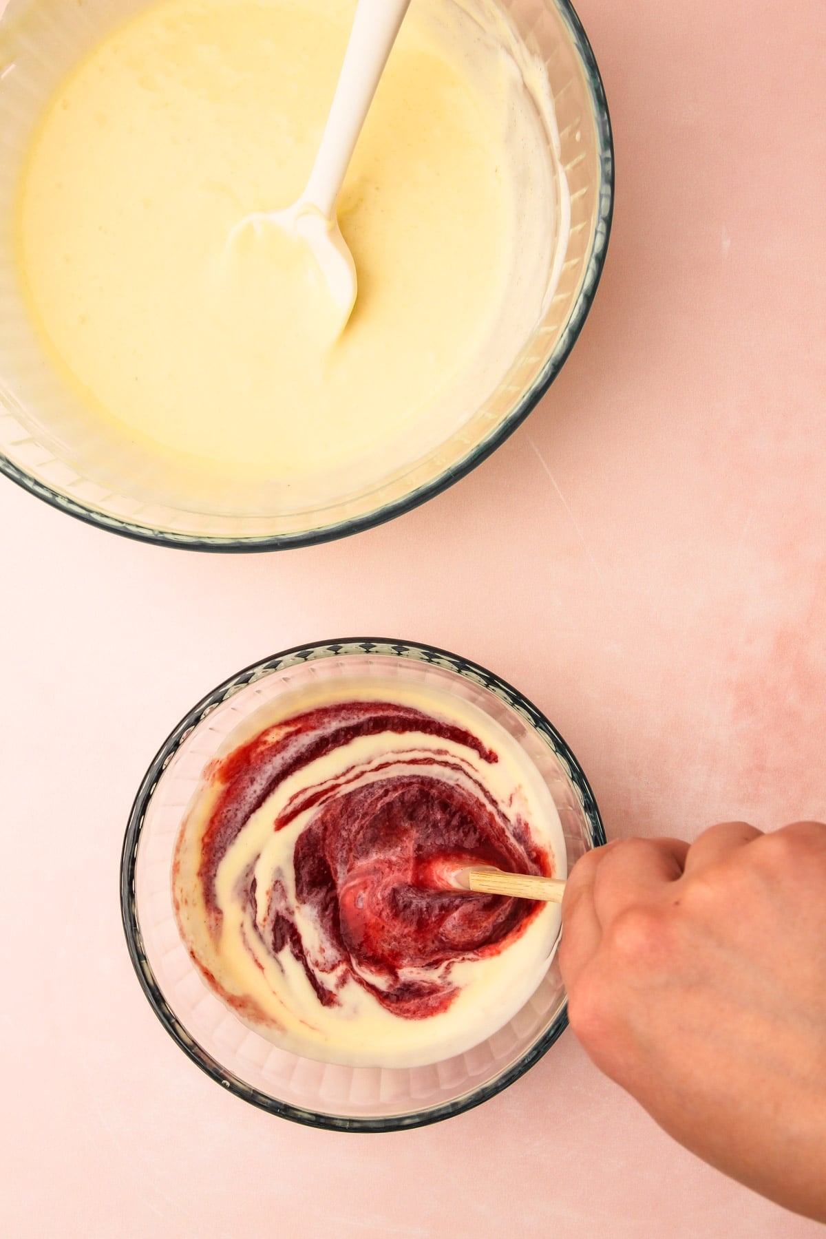 A hand using a rubber spatula to stir mascarpone filling into a bowl of roasted plum puree for roasted plum pie.