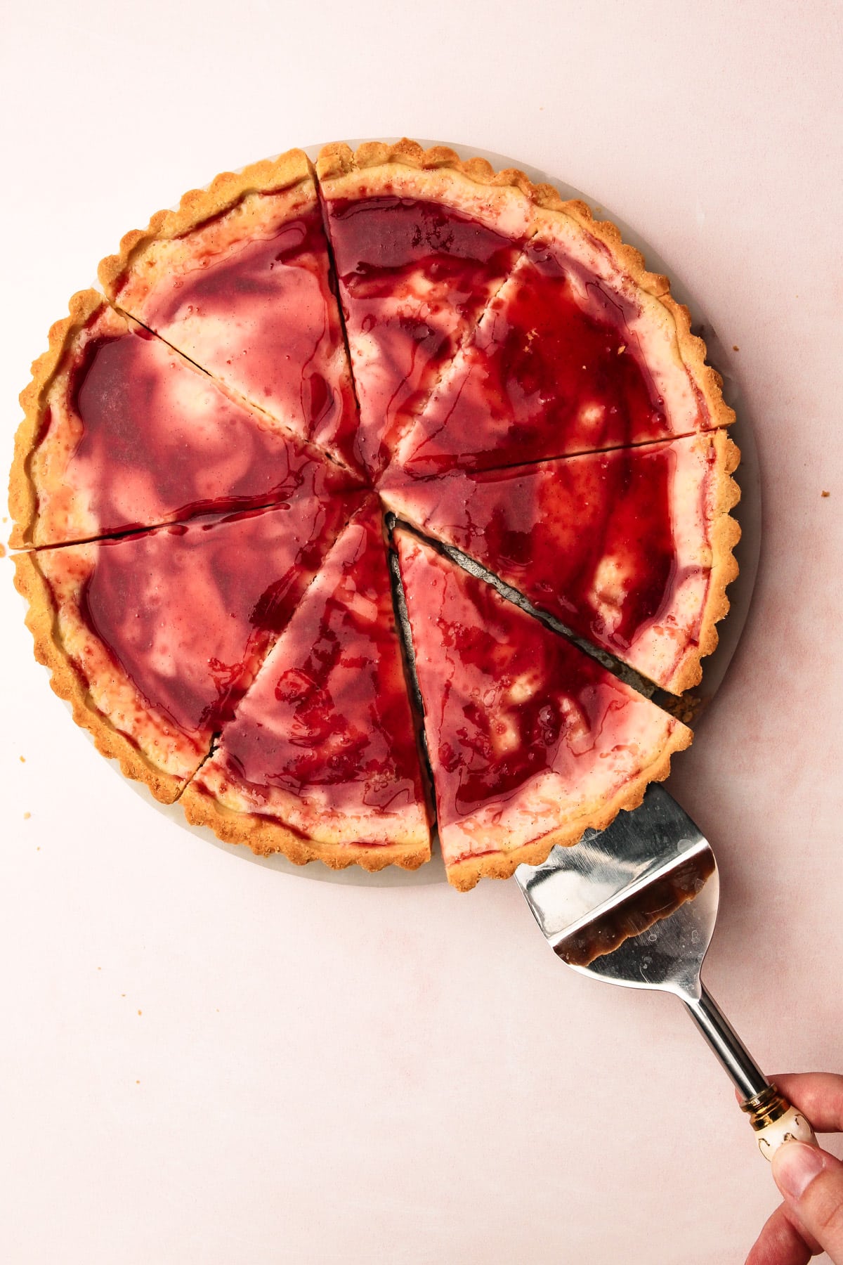 A hand using a pie server to take a slice of roasted plum pie.