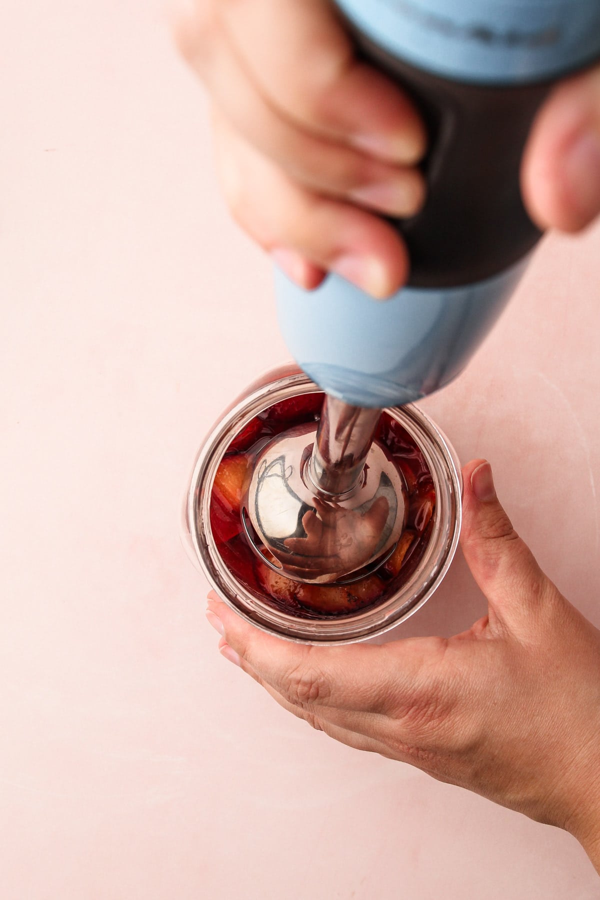 A hand using an immersion blender to blend roasted plums in a jar for roasted plum pie.