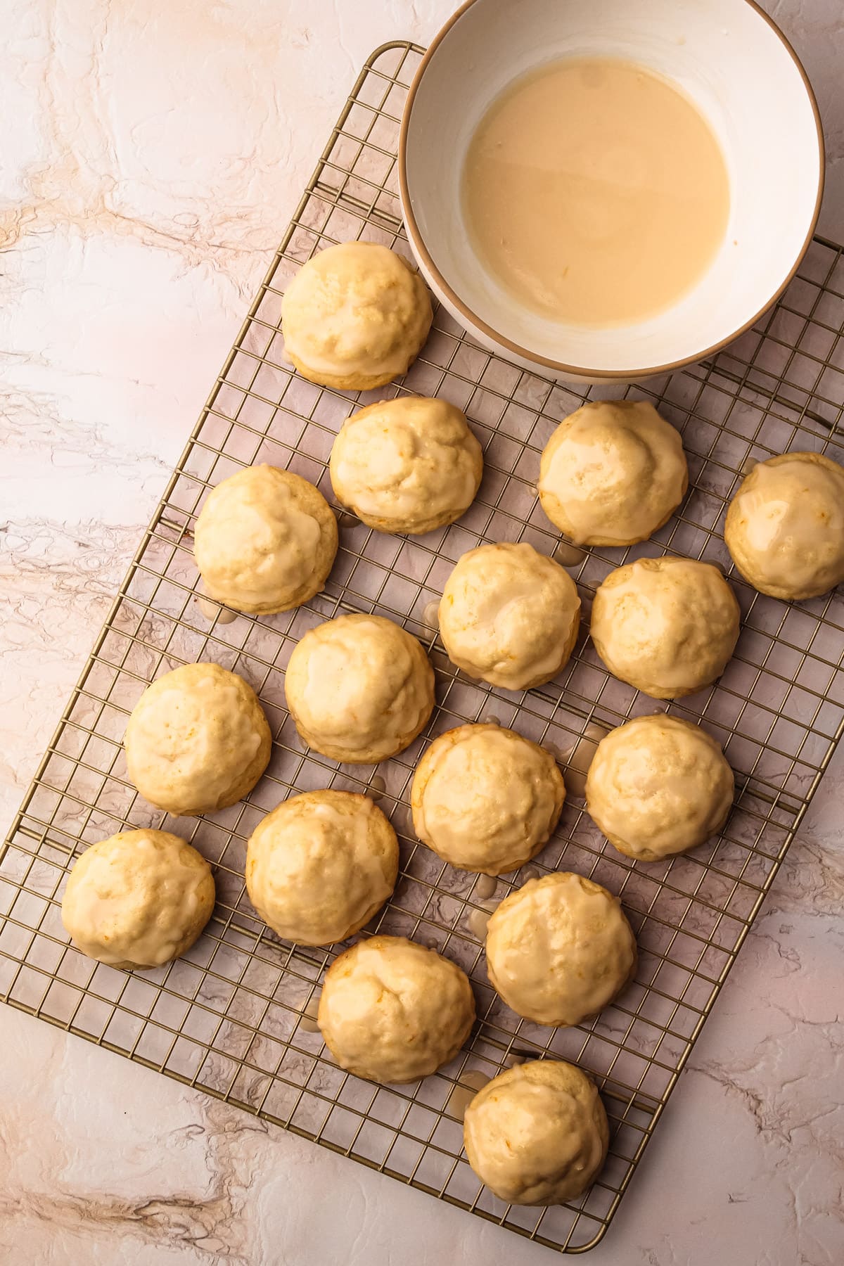 Baked soft orange cookies on a cooling rack next to a bowl of orange glaze.