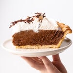 A slice of chocolate french silk pie on a plate piled high with whipped cream.