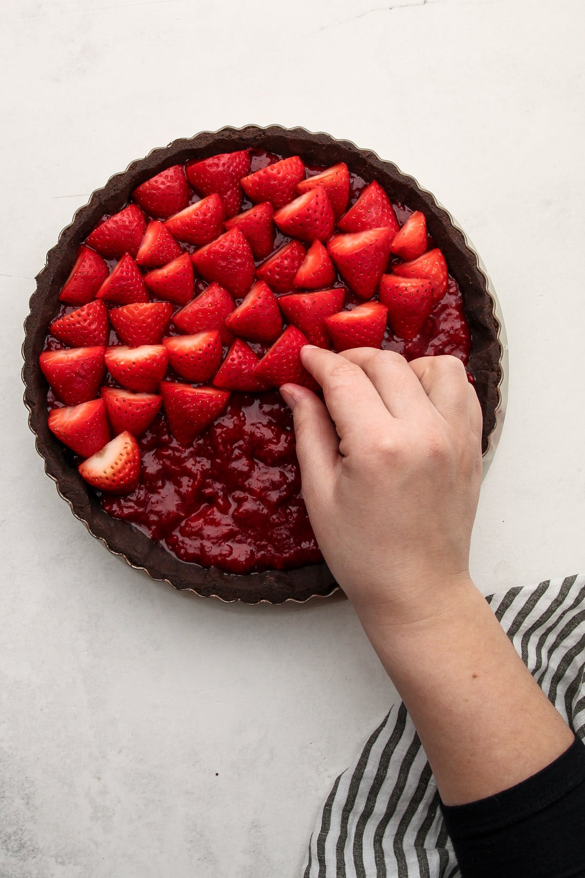 A hand arranging strawberries on the top of a chocolate strawberry pie.