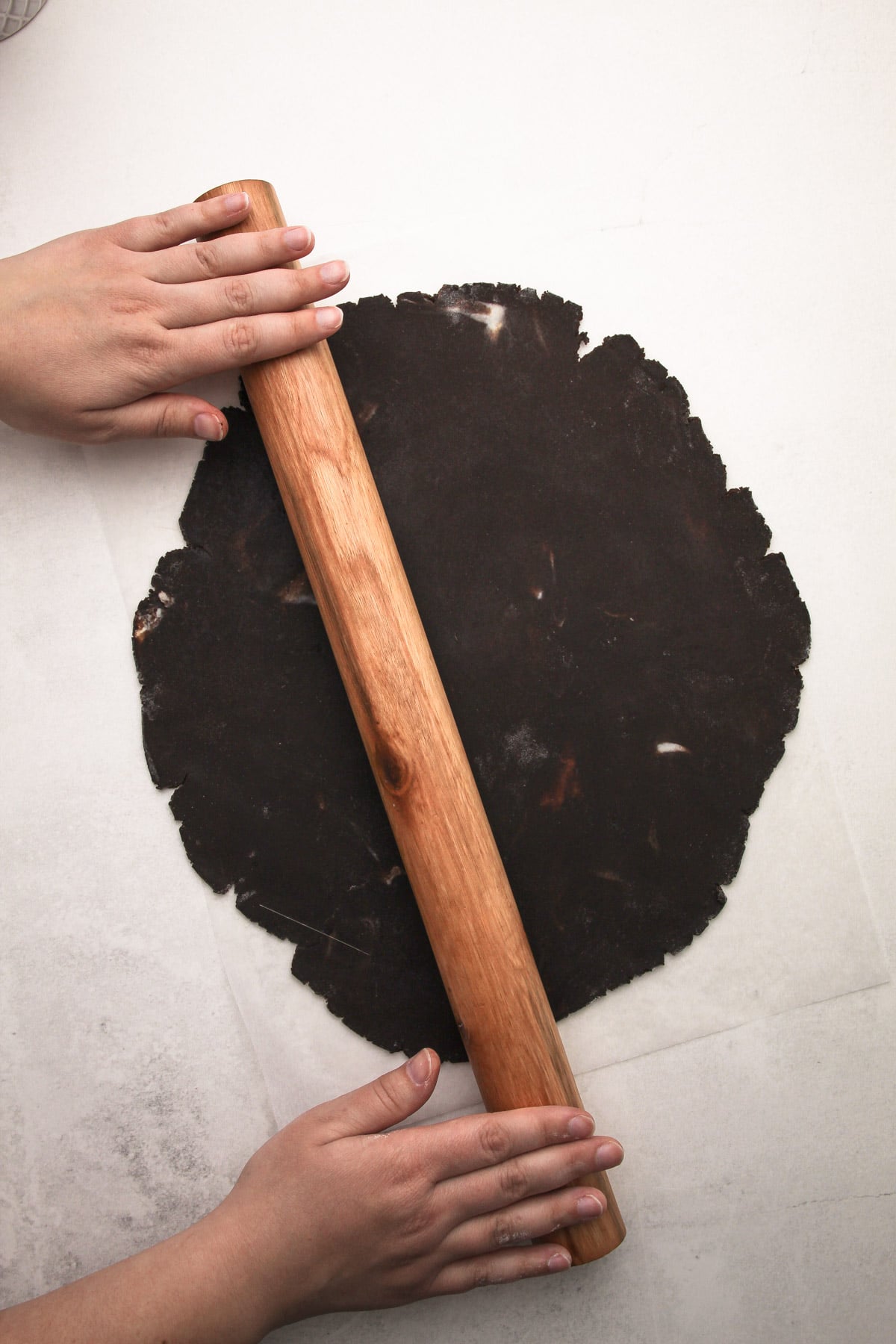 Hands using a rolling pin to roll out dough for chocolate strawberry tarts.