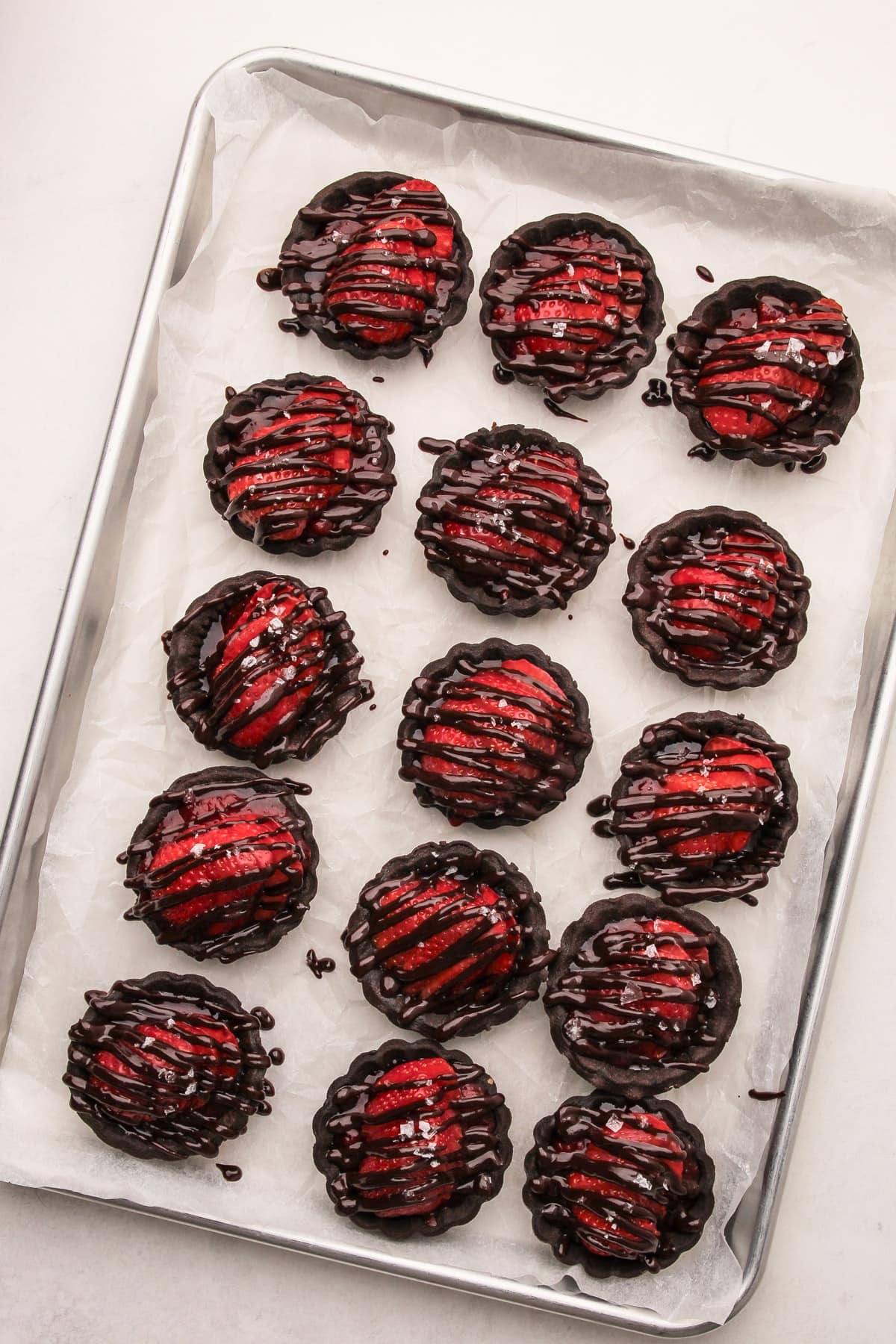 A tray of chocolate strawberry tarts that have been drizzled with melted chocolate.