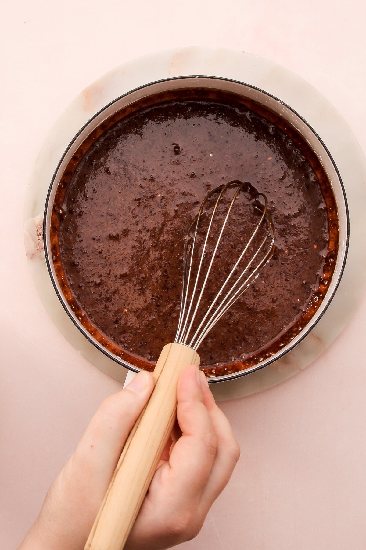 A hand whisking together ingredients for dark chocolate pudding in a saucepan.