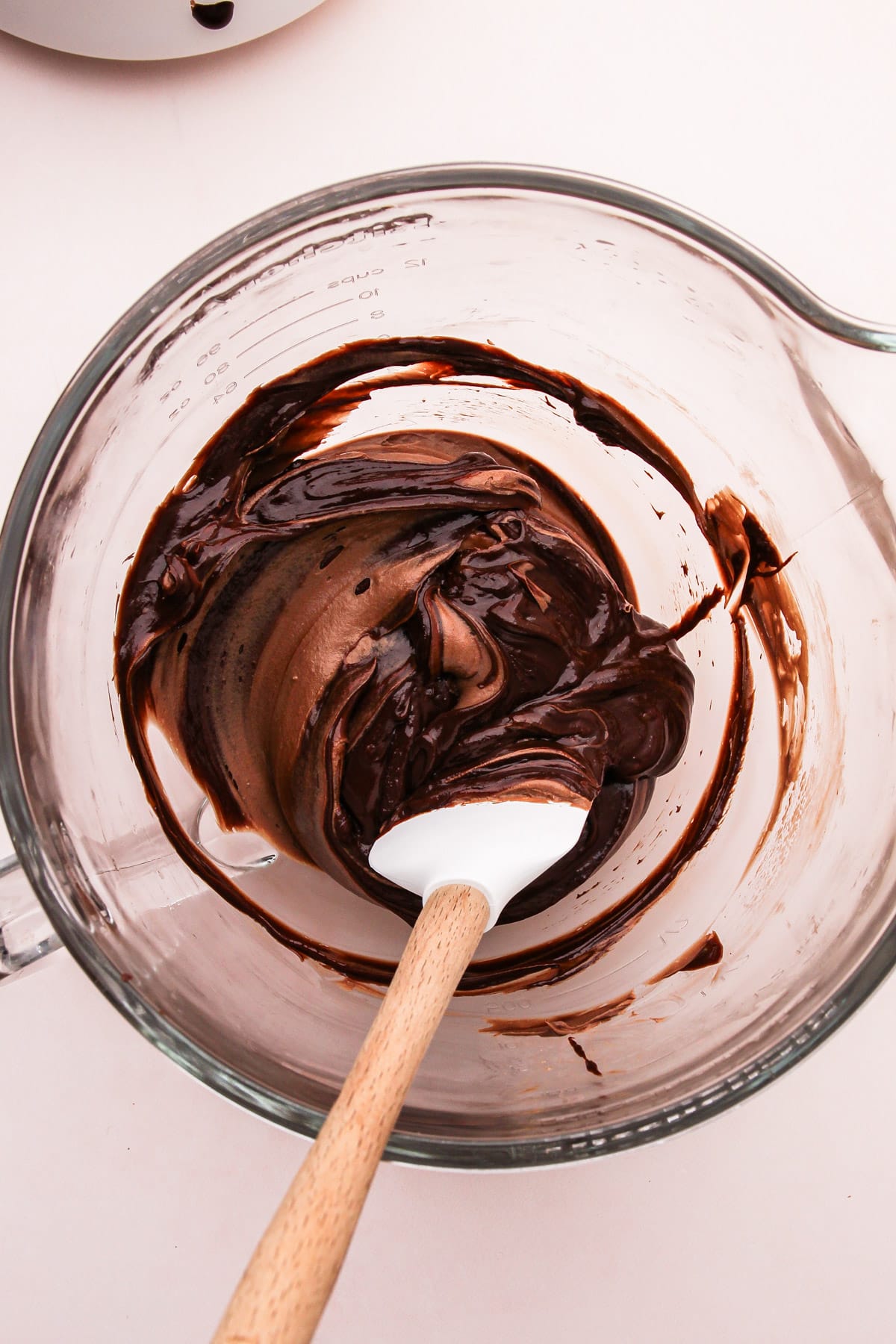 Whipped chocolate filling and melted chocolate being stirred together in a stand mixer bowl with a spatula for easy chocolate pie.