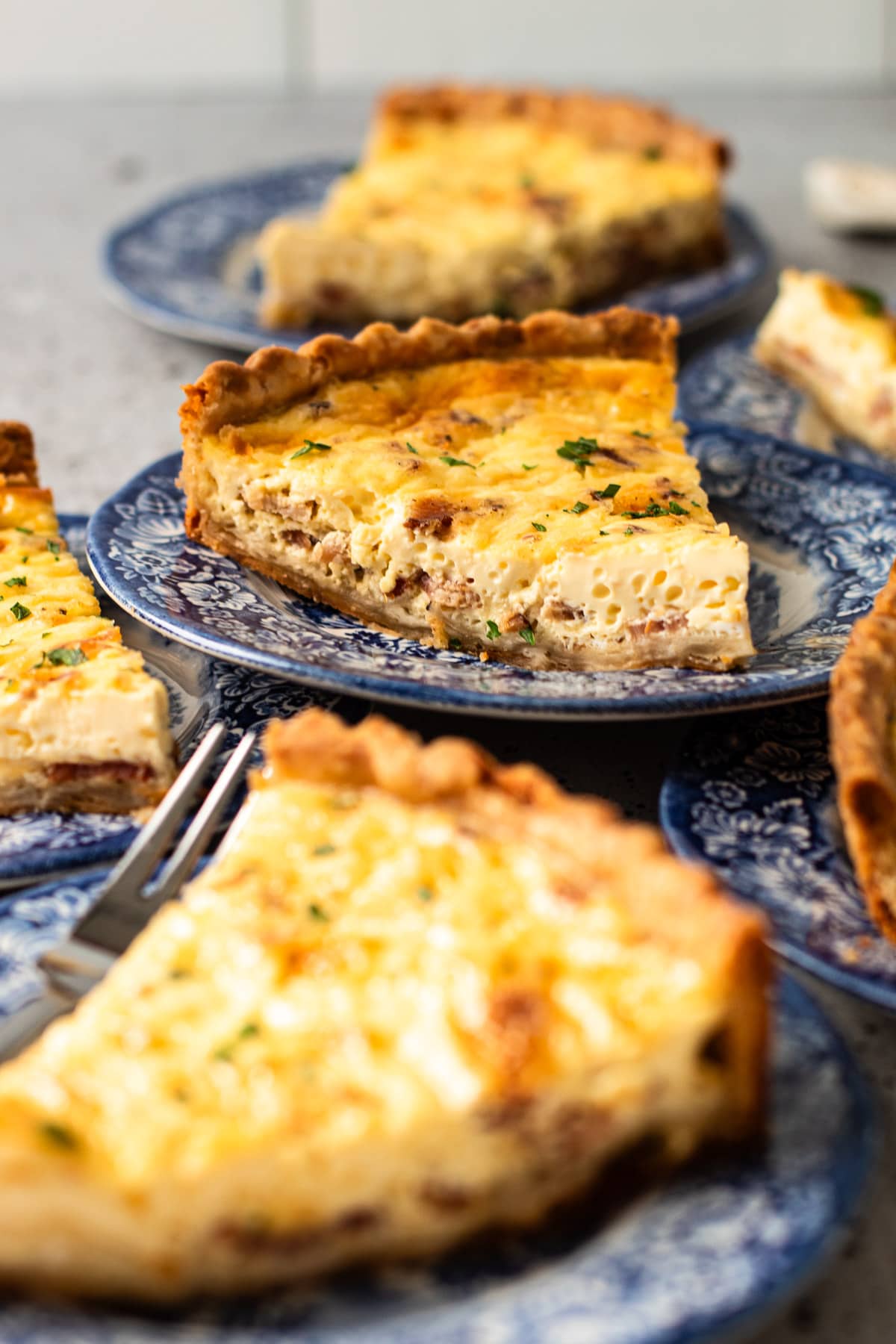 A slice of a quiche lorraine stacked with others on a blue plate.