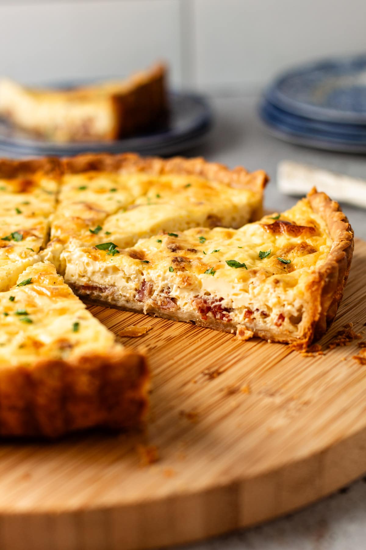 A slice of quiche lorraine on a wooden cutting board.