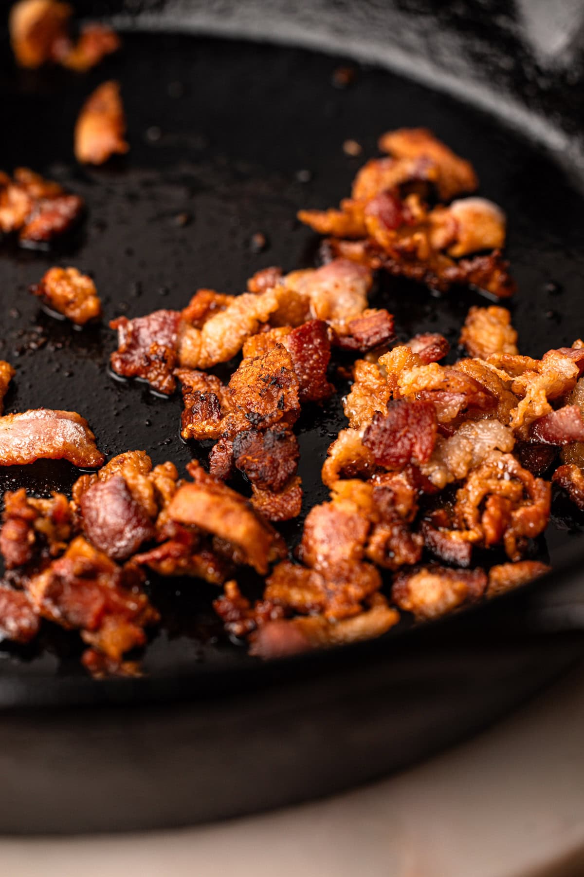 Crispy bacon cooking in a cast iron skillet.