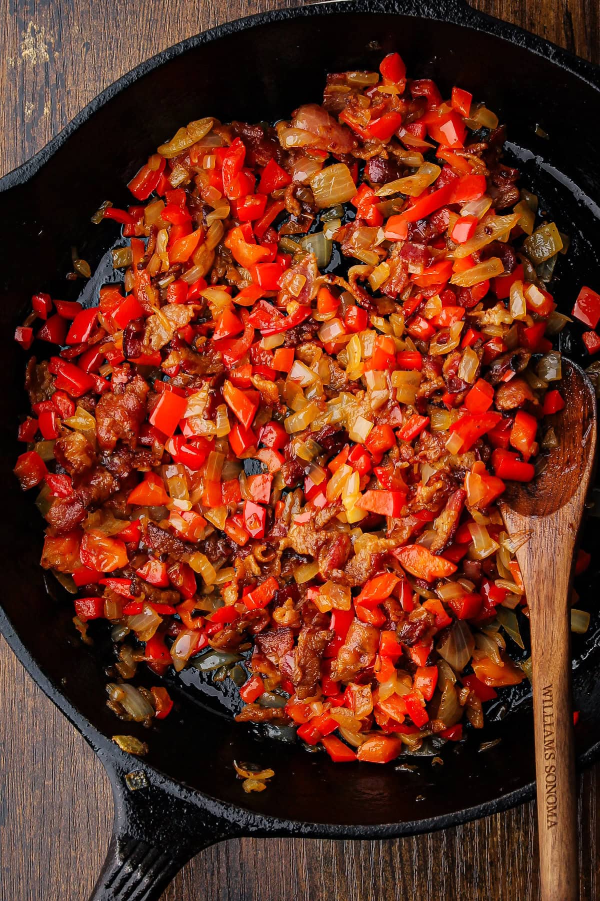 Bacon, peppers and onions cooking in a cast iron skillet.