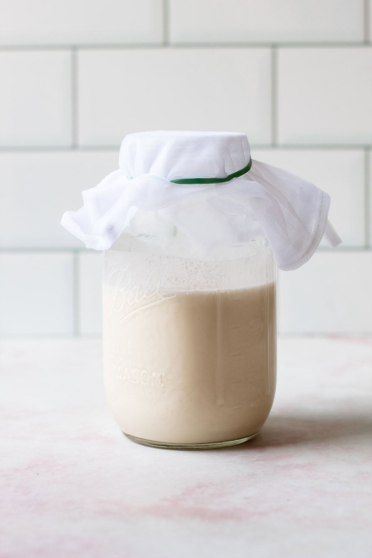 A mason jar with homemade creme fraiche with a piece of cheesecloth covering the opening.