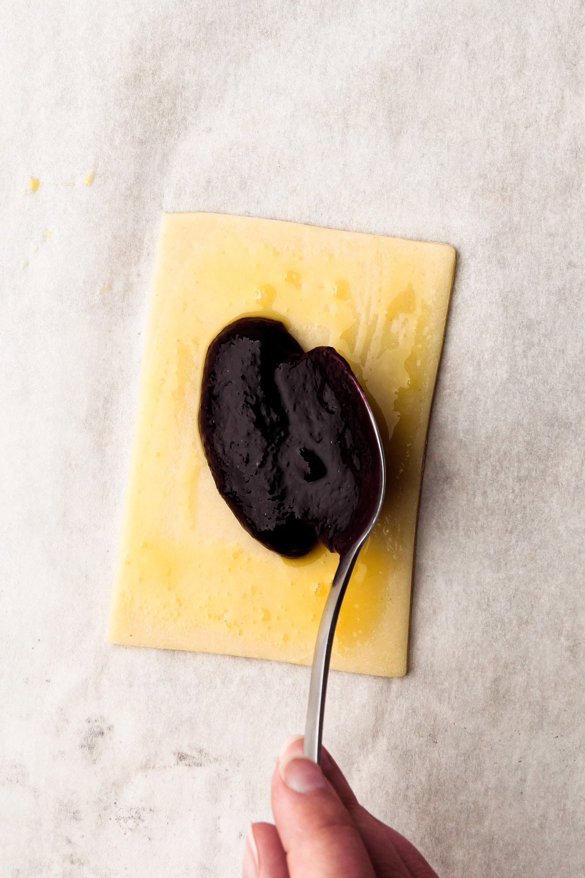 Spooning a berry filling onto a piece of pastry with egg wash.