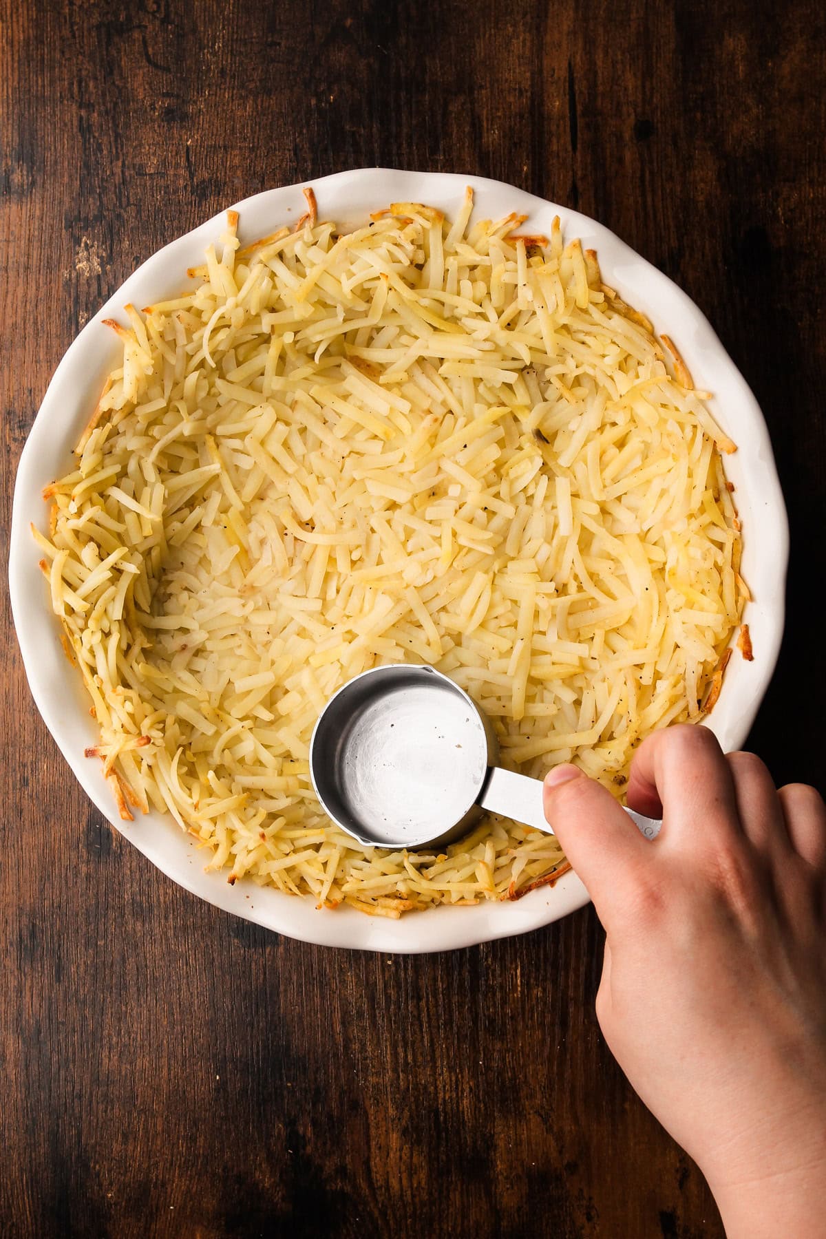 Pressing down frozen hashbrown potatoes for a pie crust.