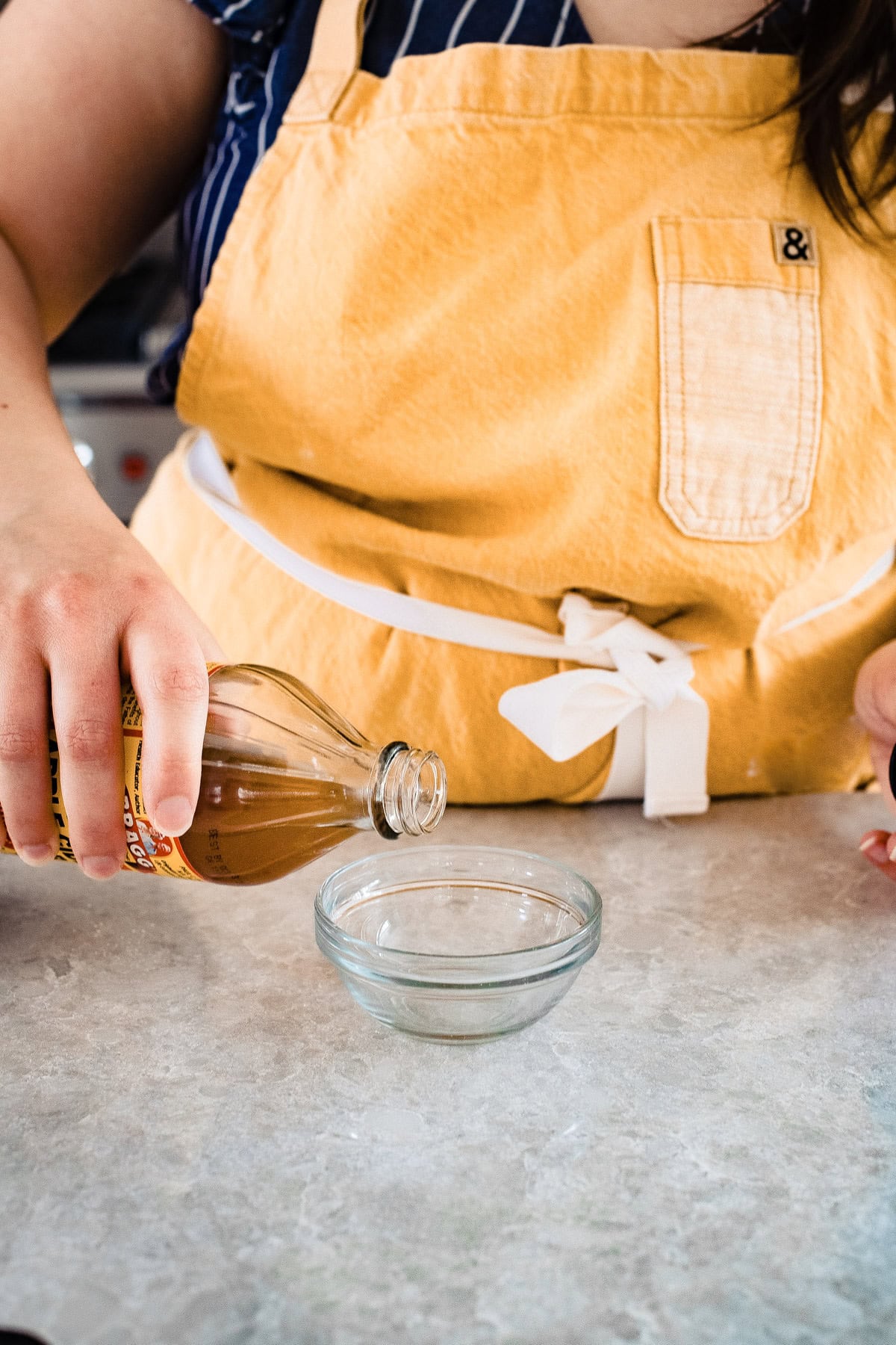 A person wearing an apron pouring vinegar into a bowl.