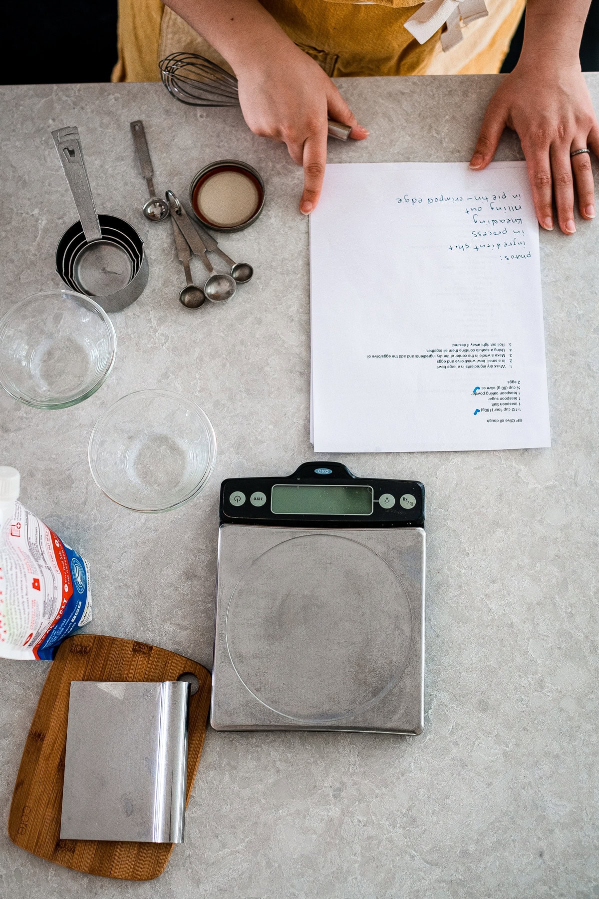 A recipe on a counter with measuring cups, spoons and a digital kitchen scale.