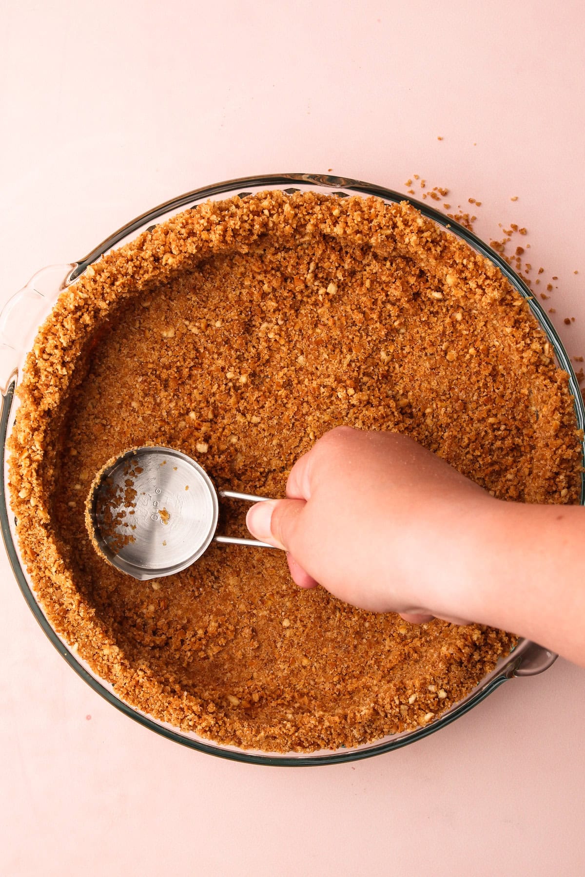 Forming a graham cracker crumb crust in a pie plate using a measuring cup.