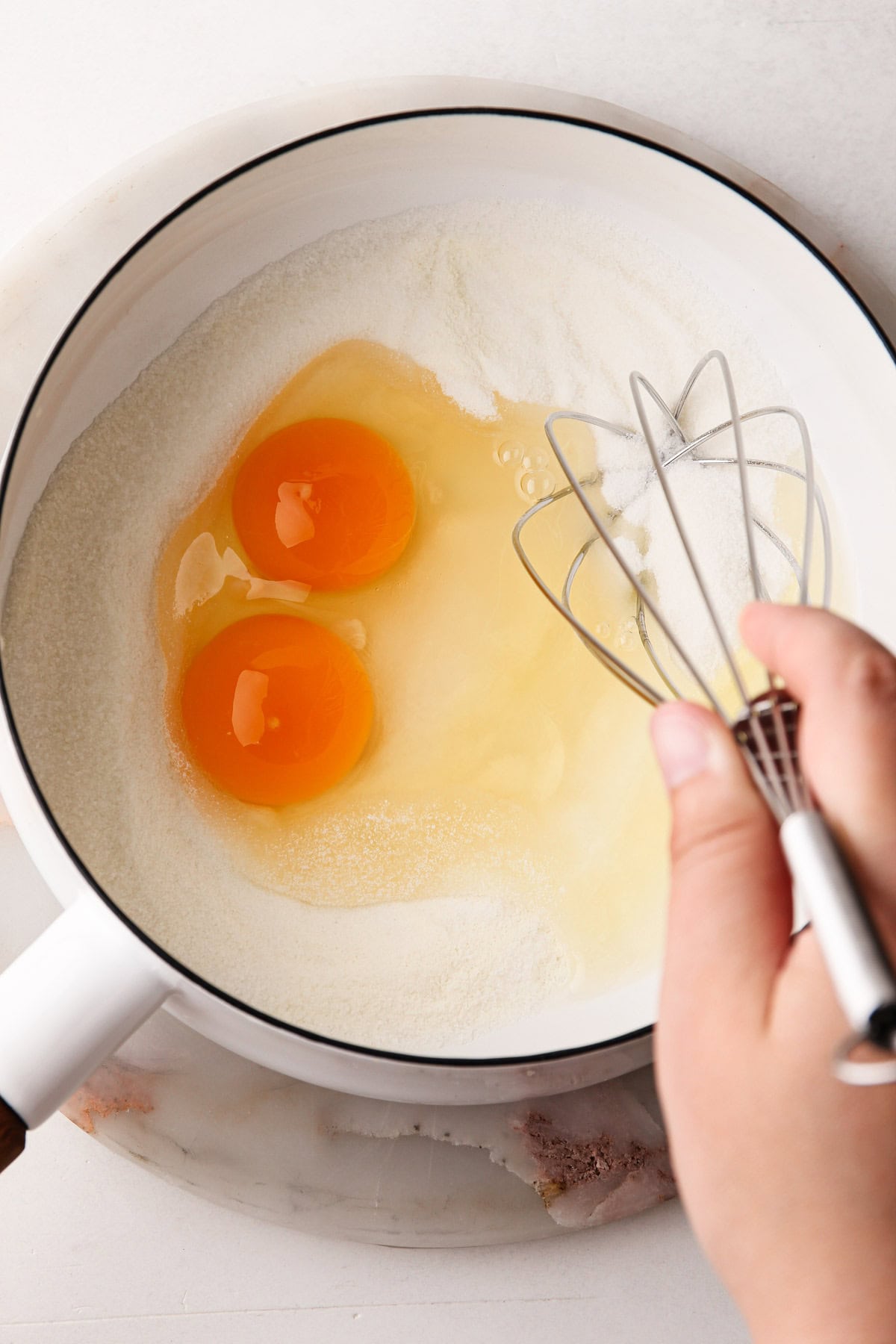 Eggs and sugar in pot with a whisk.