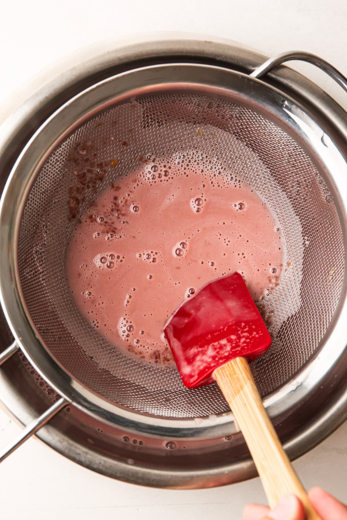 Straining a cherry custard ice cream base through a strainer.