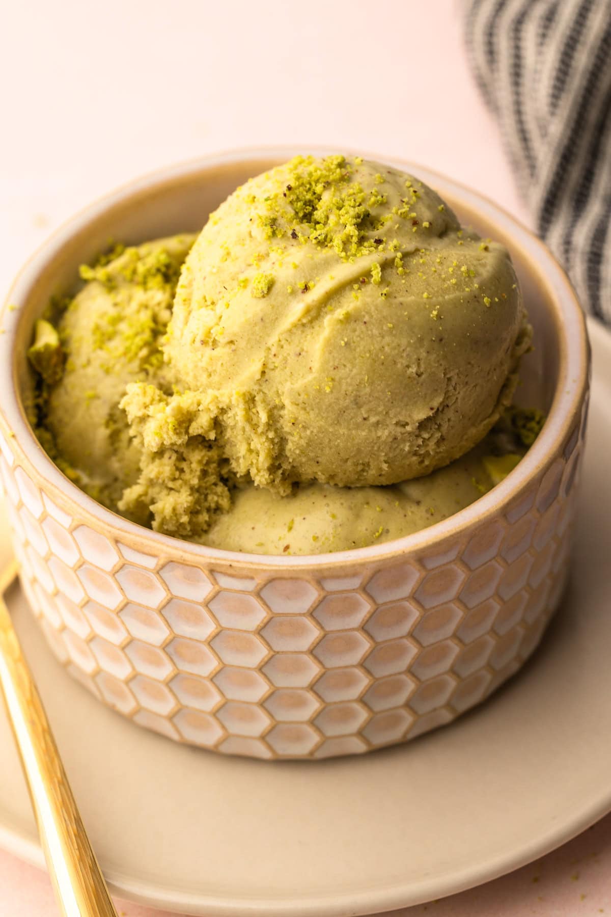 A serving of pistachio ice cream with a sprinkle of pistachios on top in a small bowl.