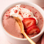 A serving of strawberry pudding with whipped cream and fresh sliced strawberries.