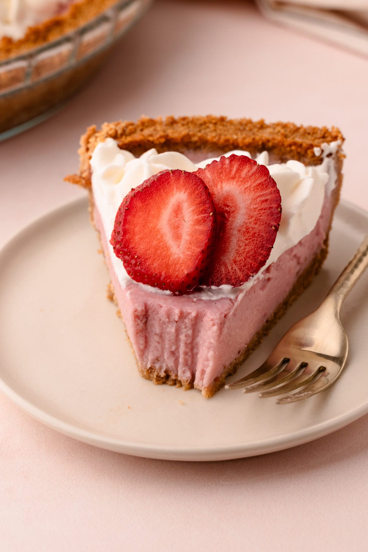 A strawberry cream pie slice on a plate with a bite taken from it.