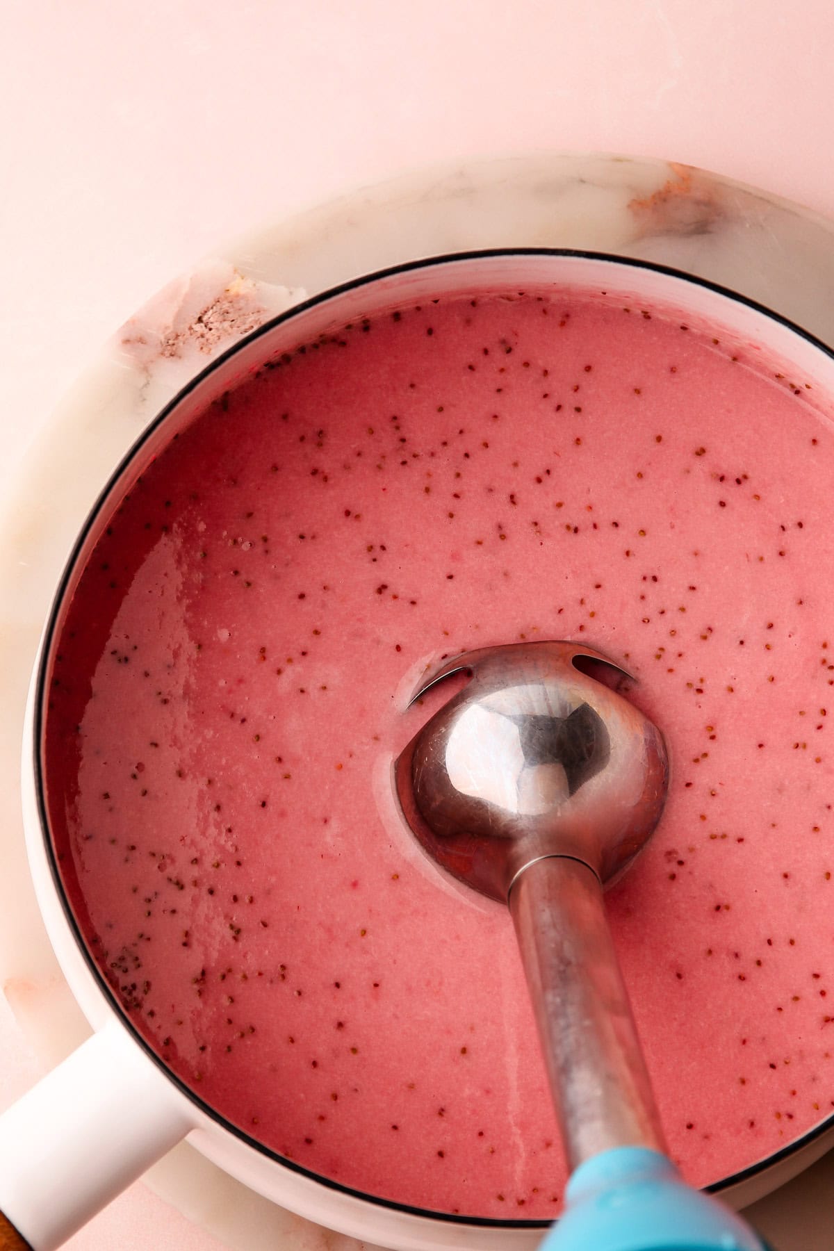 A gelatin set strawberry cream mixture in a pot getting blended with a stick blender.