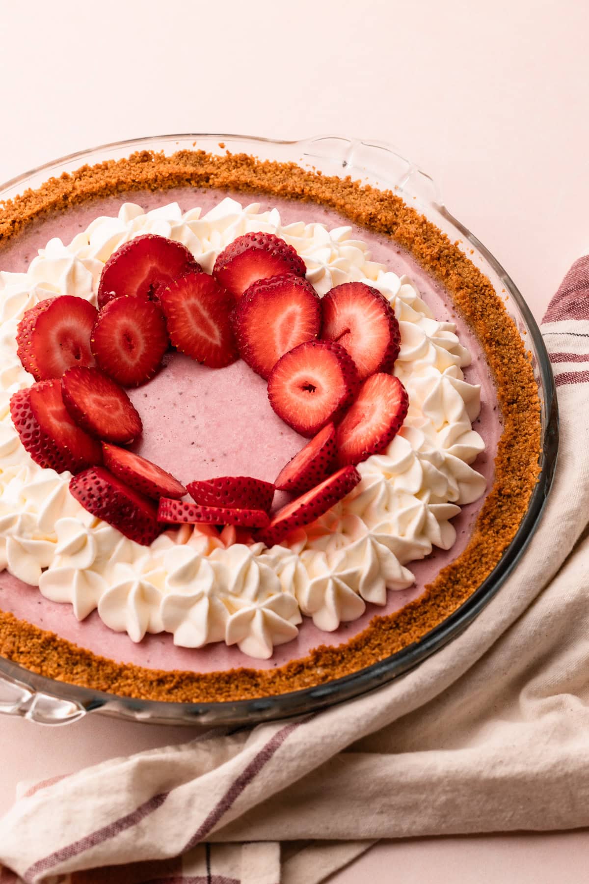 A strawberry cream pie in a crumb crust with whipped cream and fresh strawberries.