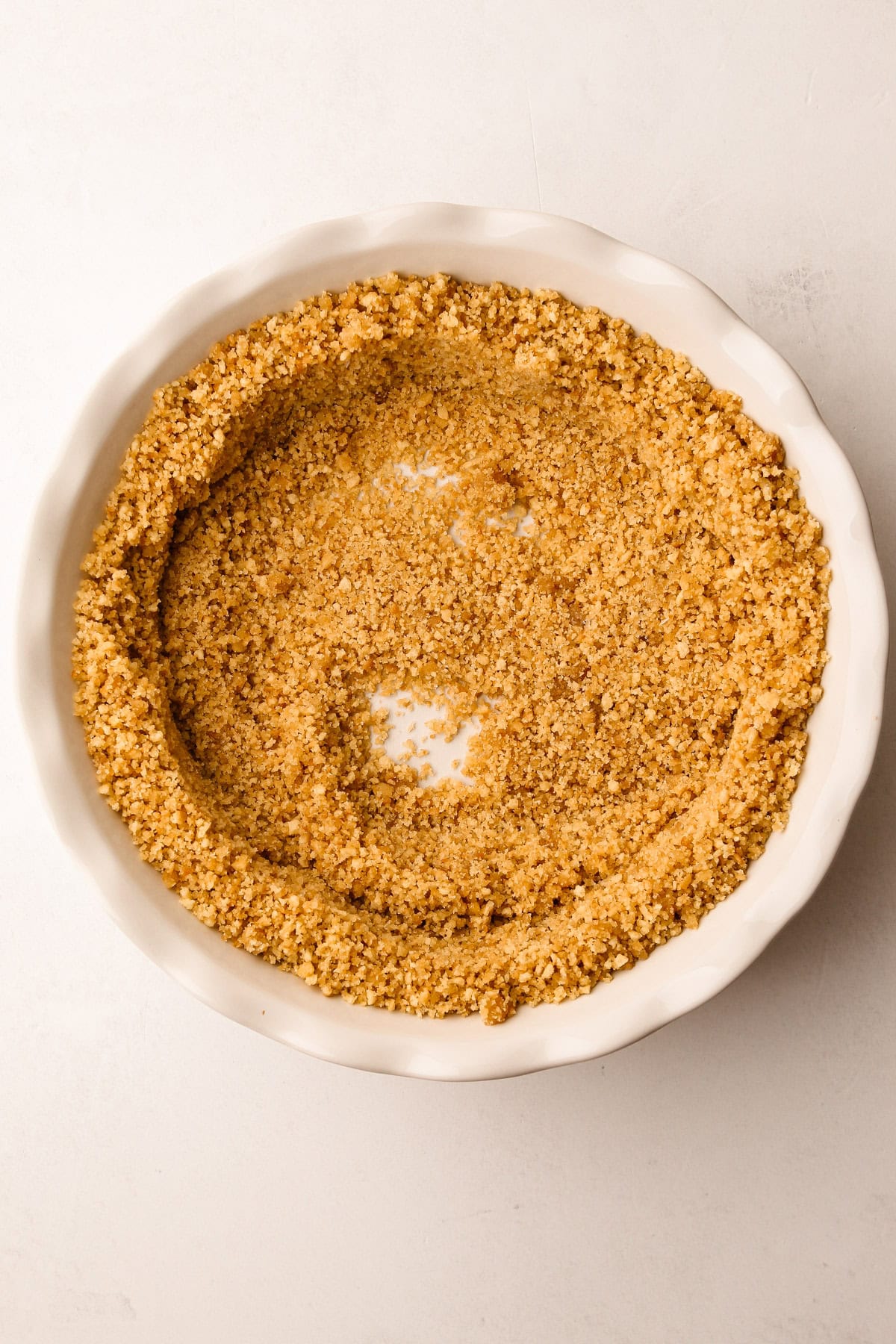 A vanilla wafer crumb crust mixture in a pie plate getting formed.