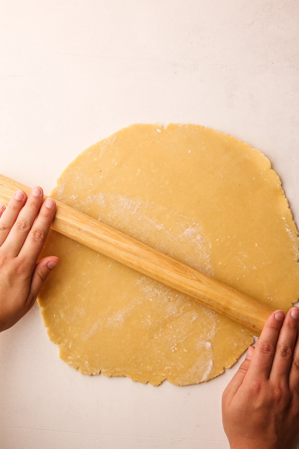 Hands rolling out tart dough with a rolling pin.