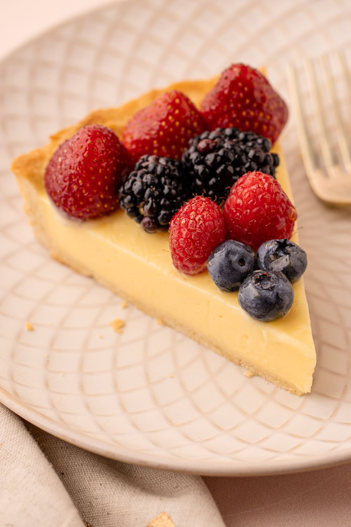 Slice of fresh fruit tart on a plate with a variety of berries.