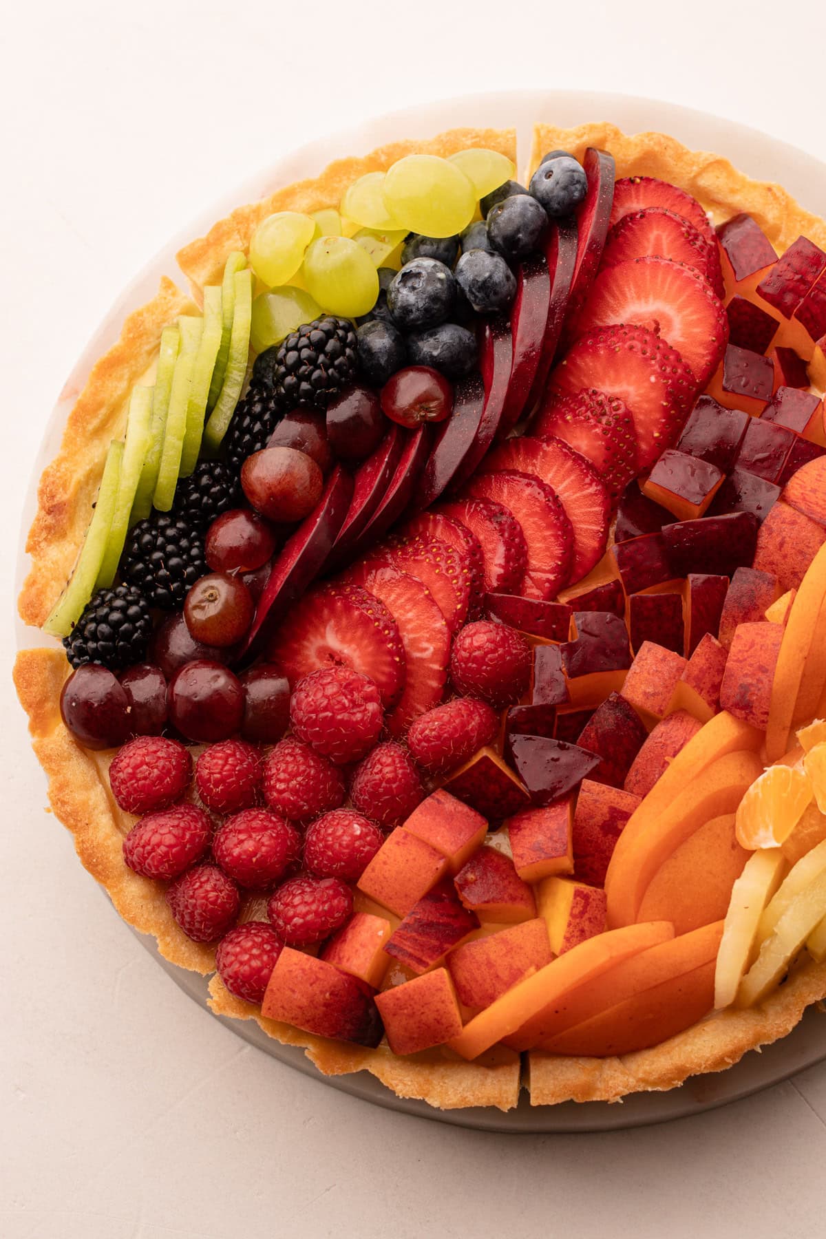 Fresh fruit tart topped with a variety of sliced fruits in a rainbow pattern.