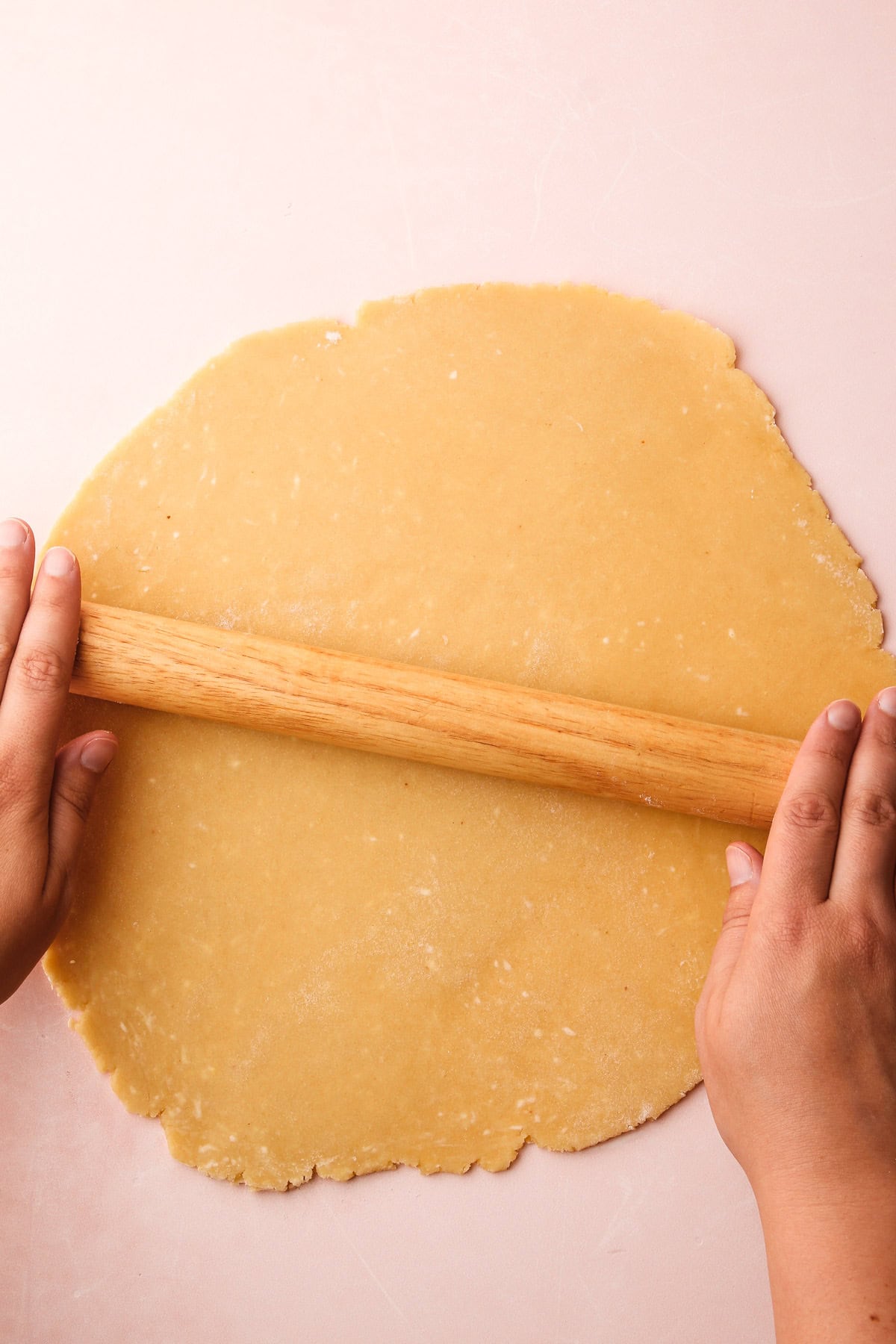 Rolling out tart dough with hands for fresh fruit tart crust.